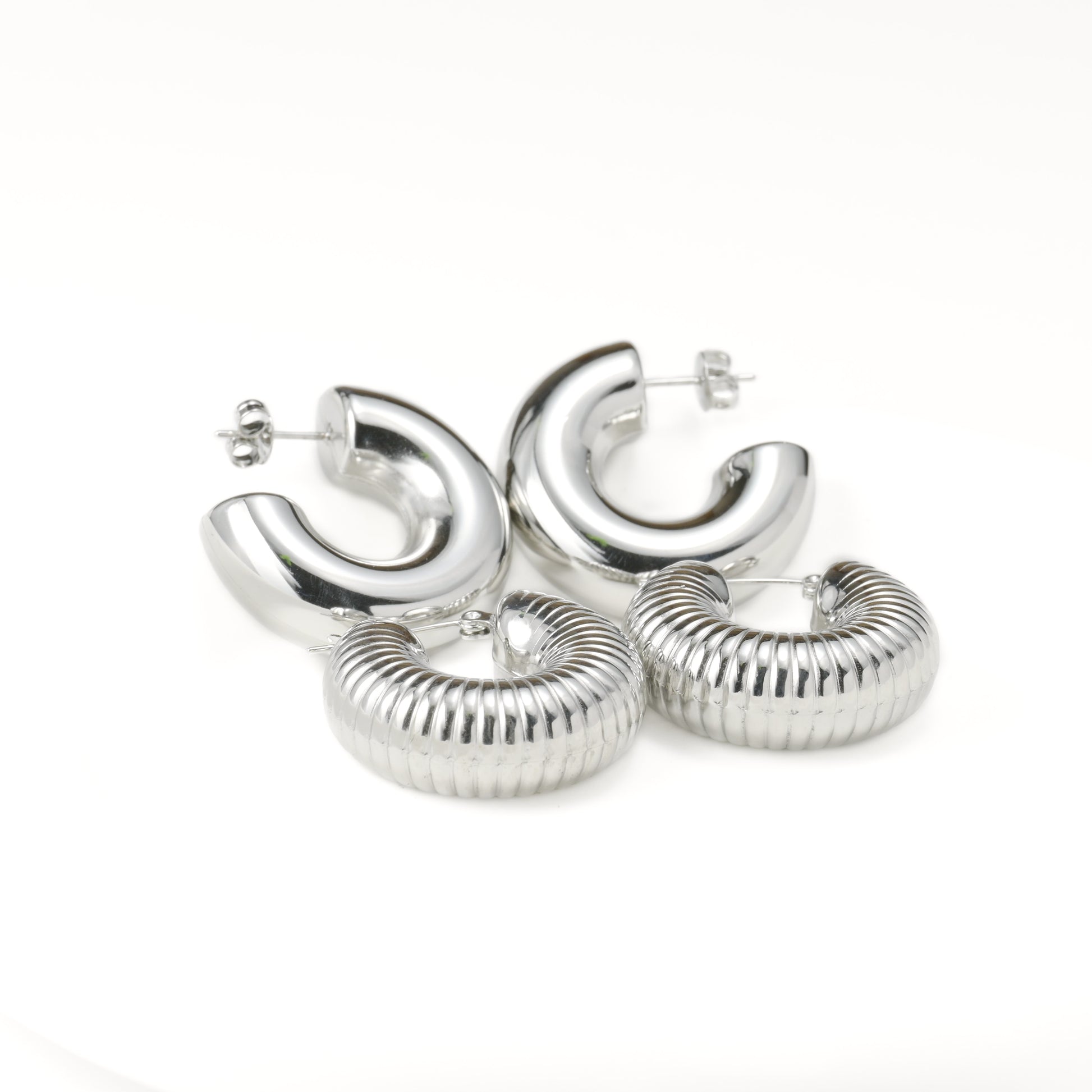 Set of thick silver hoop earrings with plain and textured designs on a white background
