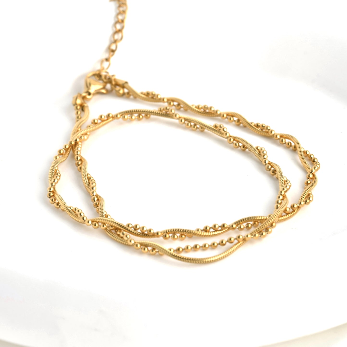 Gold snake chain necklace with integrated beads coiled on a white background