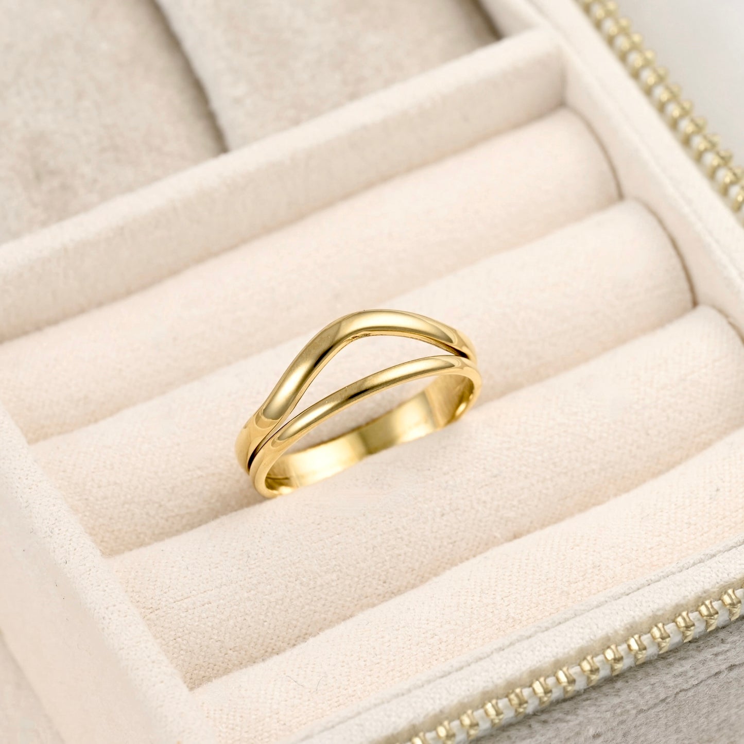 A polished gold ring with a wavy, intertwined double-band design, displayed on the cream-colored velvet compartments of a jewelry box.