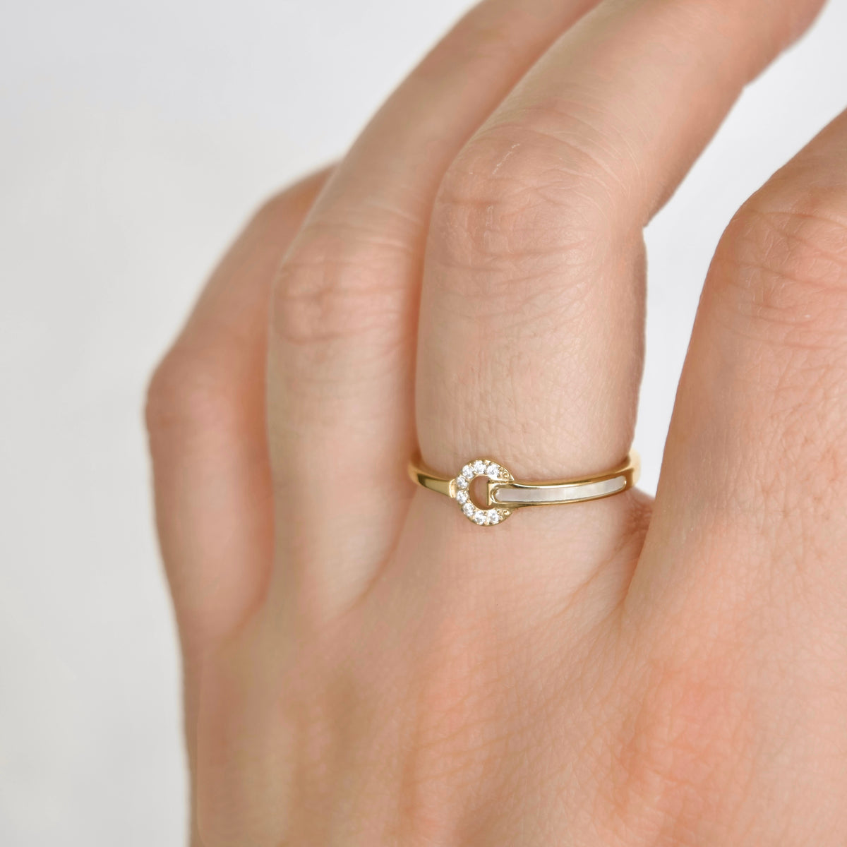 A close-up of a hand wearing a delicate gold ring with a small circular diamond halo on a plain light background.