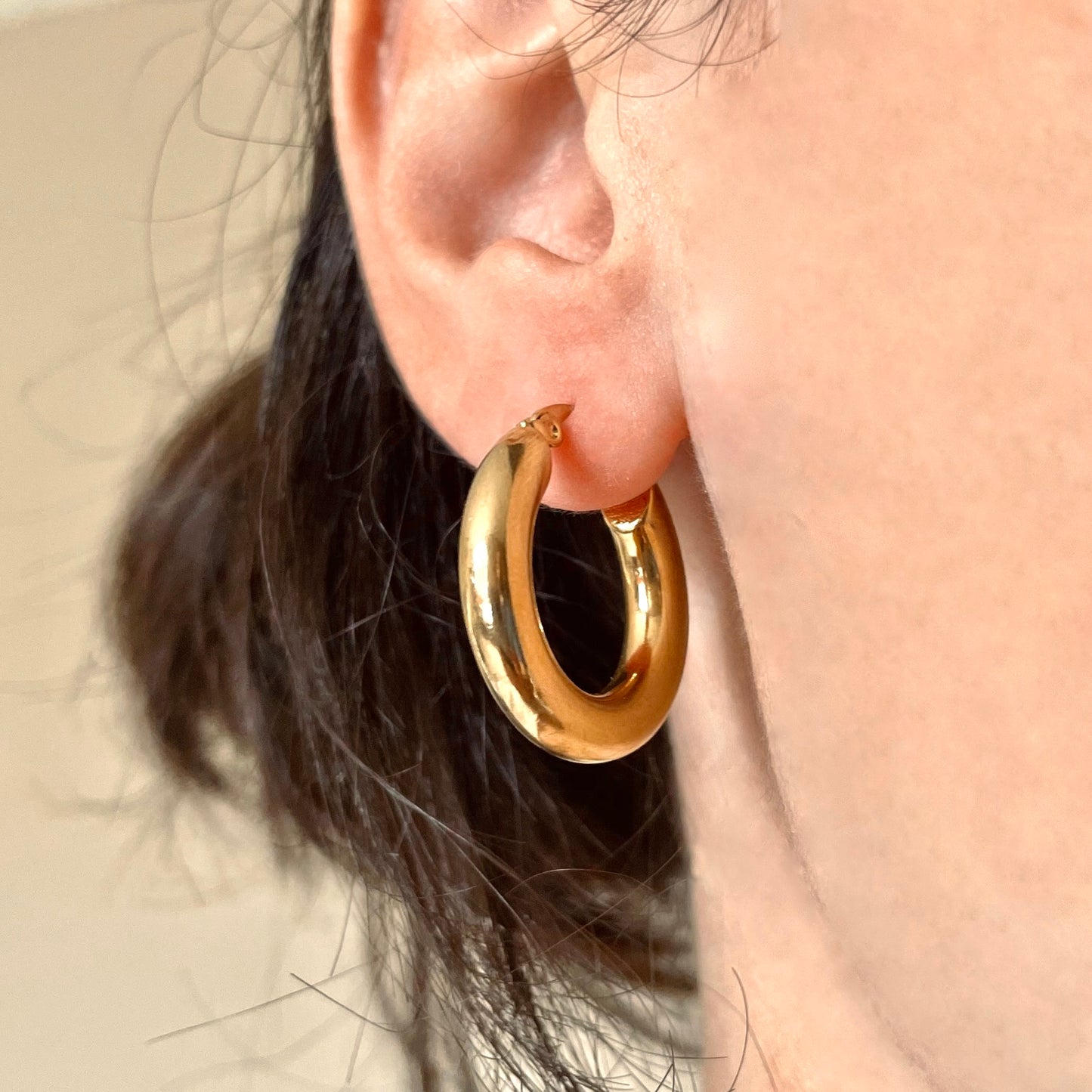 25mm thick gold hoop earrings worn by a person with a neutral background