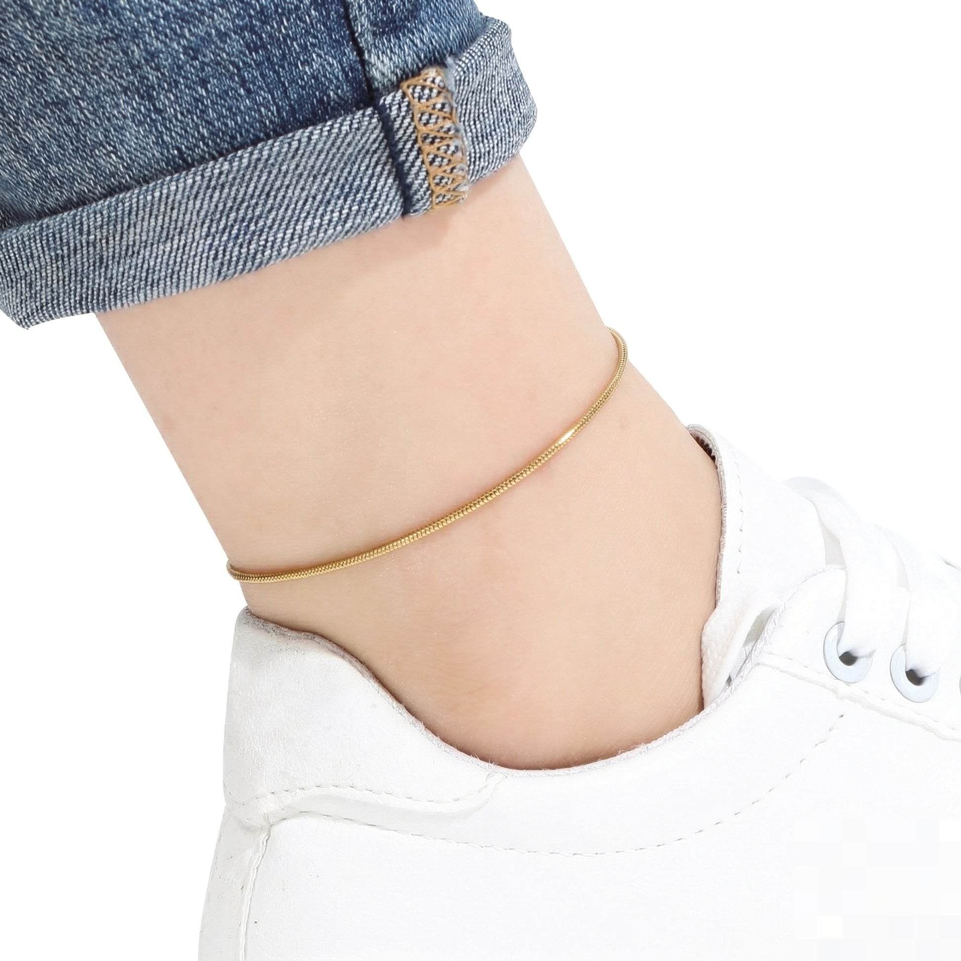 Gold snake anklet on a person's ankle with white sneakers and blue jeans.