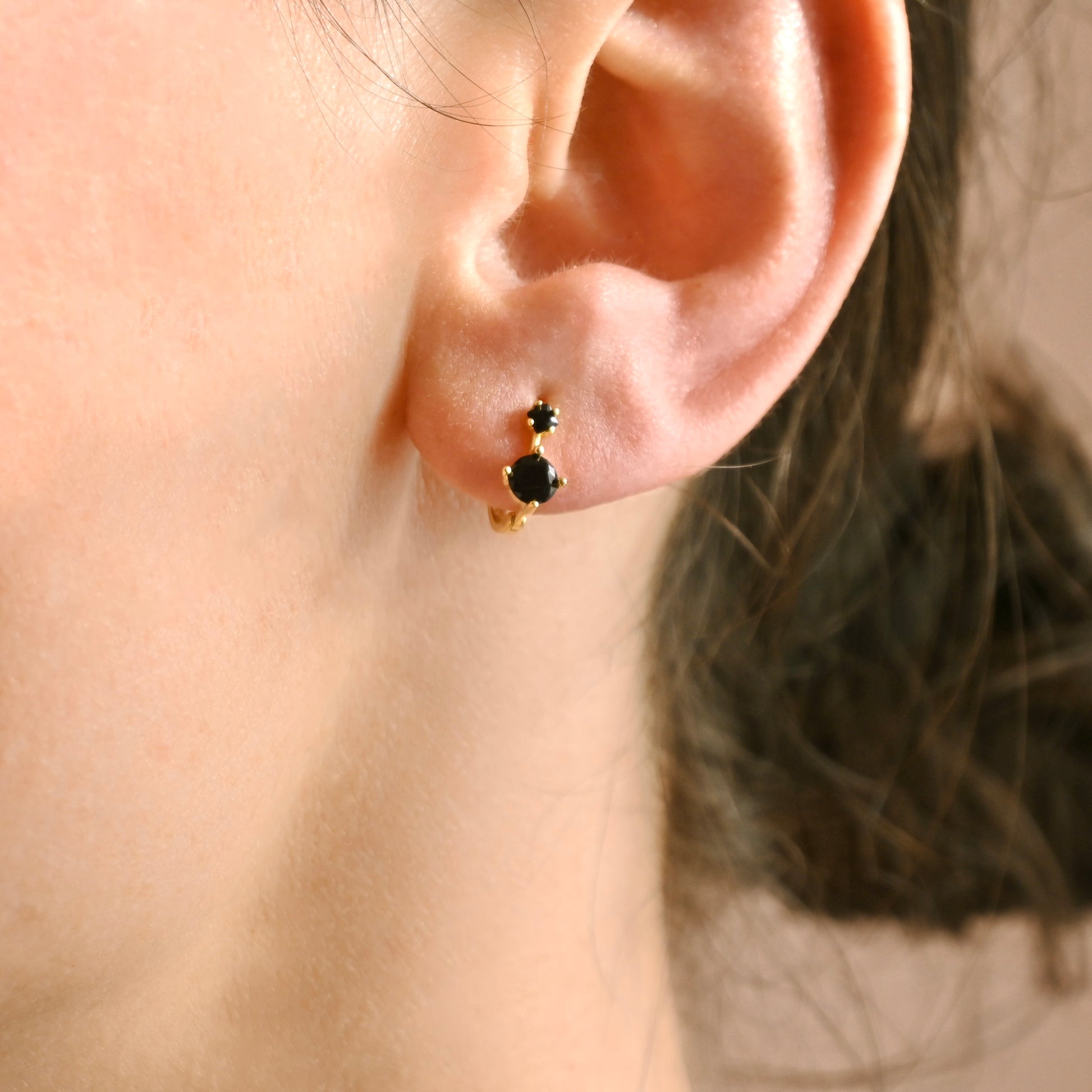Close-up of an ear wearing a gold earring with a black gemstone.