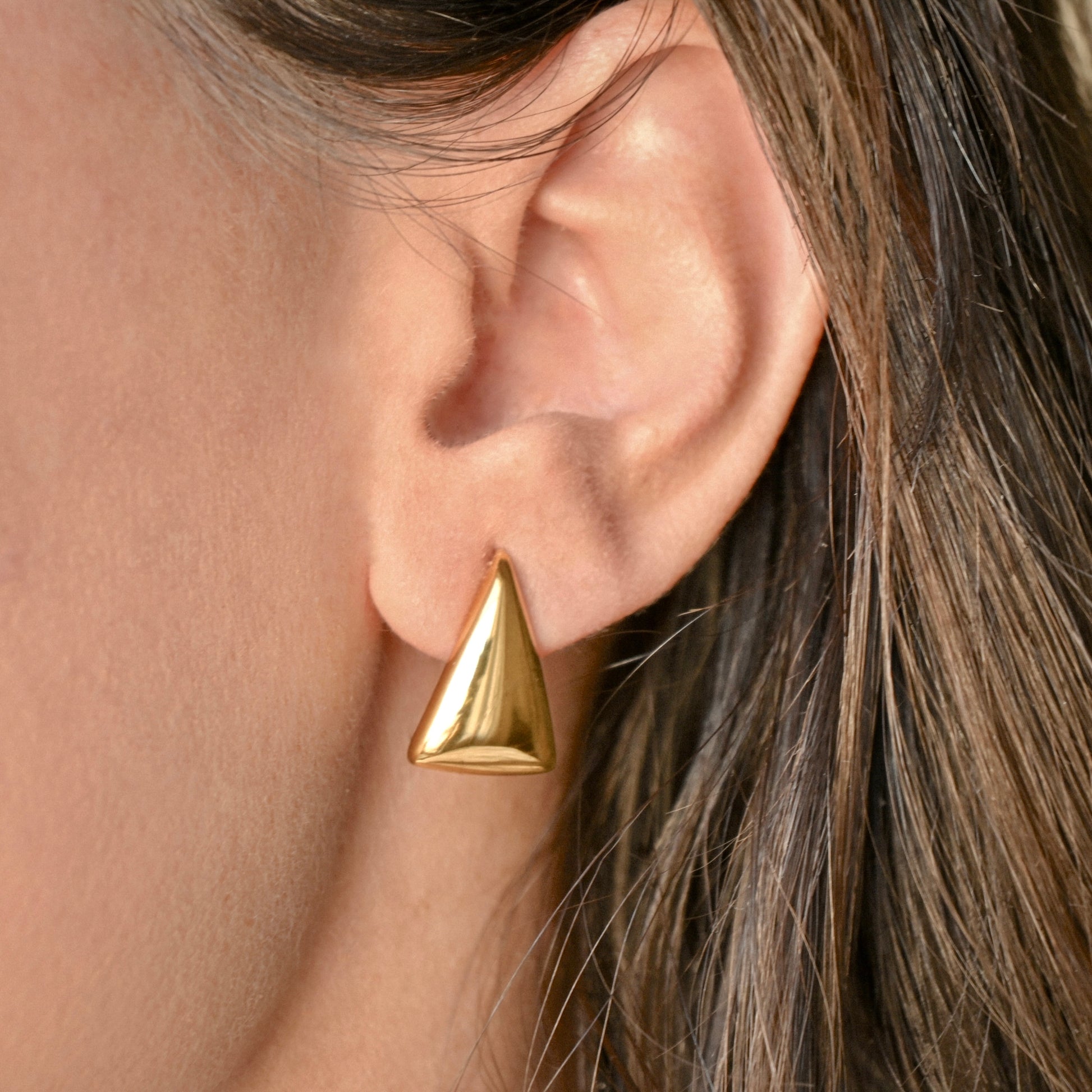 Gold geometric drop earring worn by a person with brown hair.