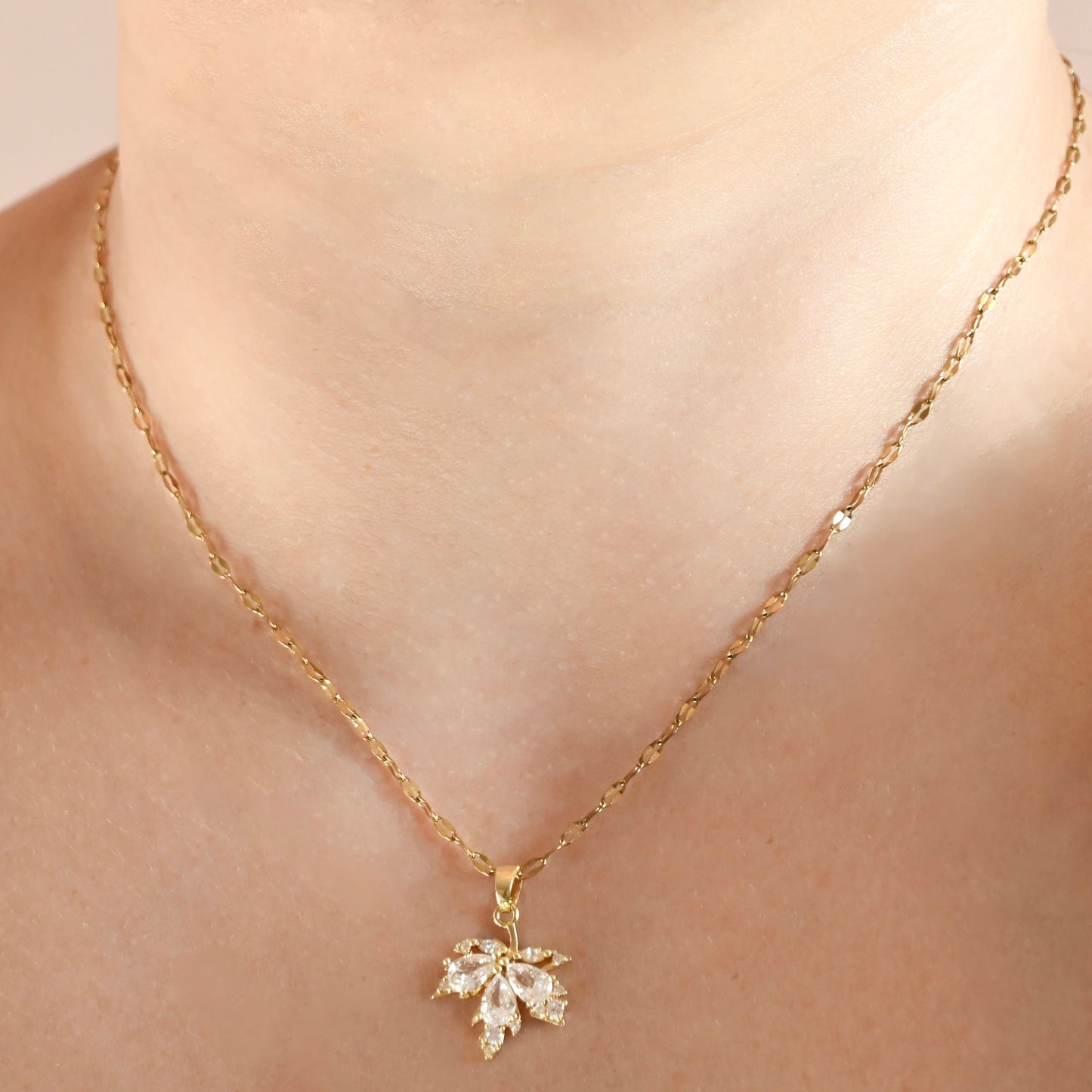 A close-up of a person's neck and collarbone wearing a delicate gold chain necklace with a small flower-shaped clear crystal pendant.