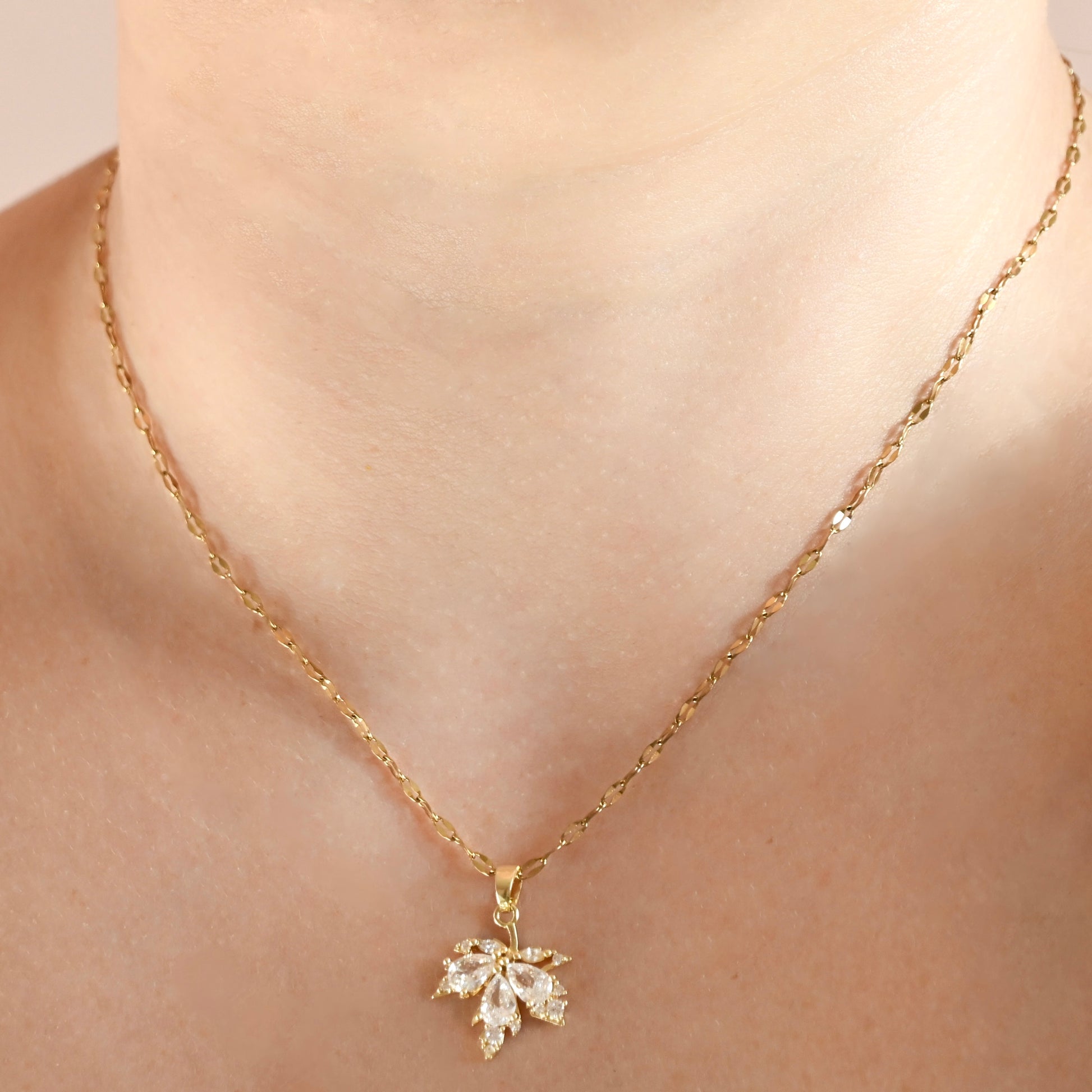 A close-up of a person's neck and collarbone wearing a delicate gold chain necklace with a small flower-shaped clear crystal pendant.