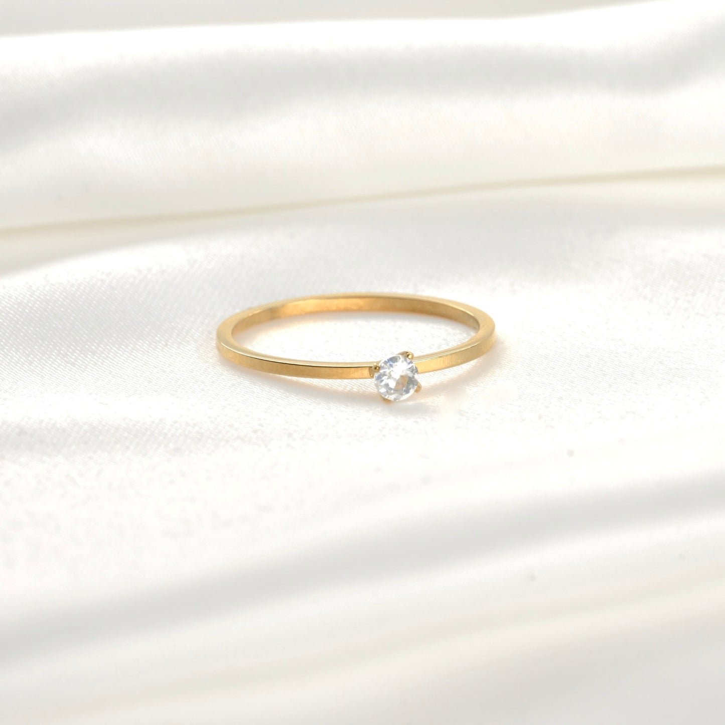 Front view of gold ring with a single small round stone on a white satin background