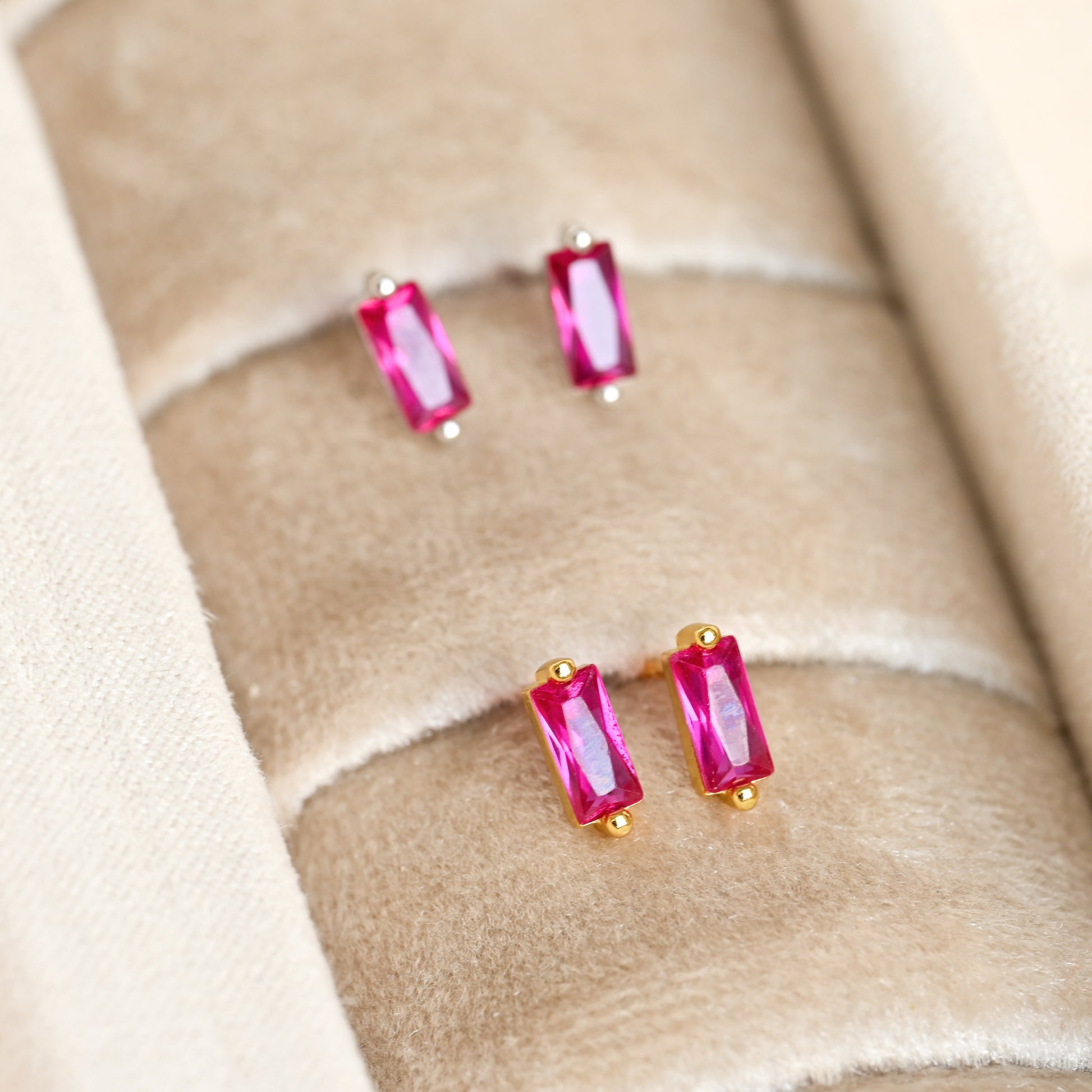 Pair of small gold and silver earrings with ruby gemstones on a beige fabric background