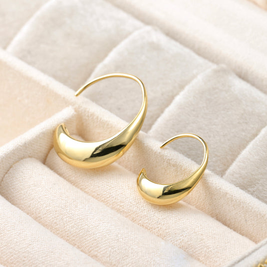 Gold  teardrop hoop earrings on a quilted beige surface