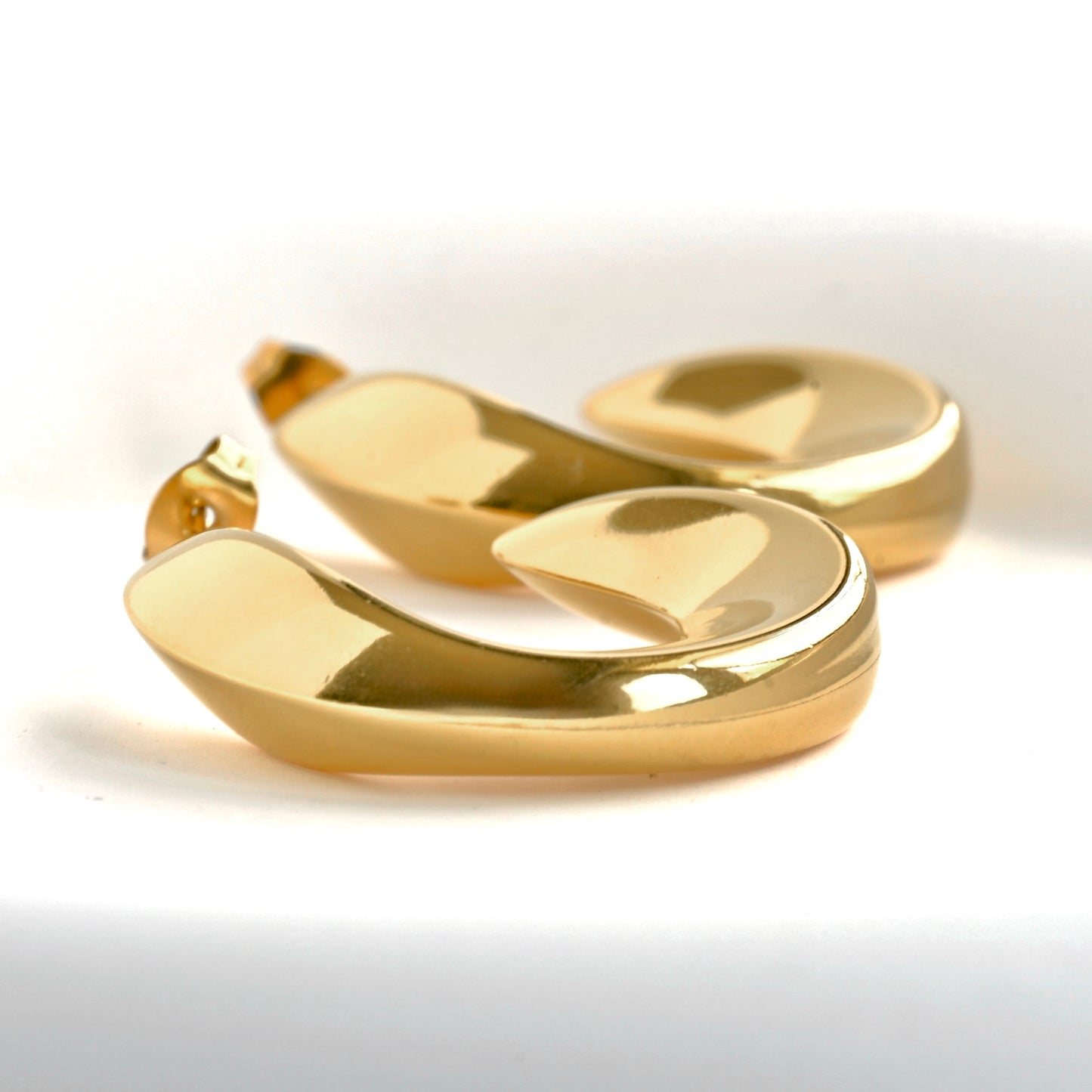 Close up side view of gold C earrings with uneven thickness.
