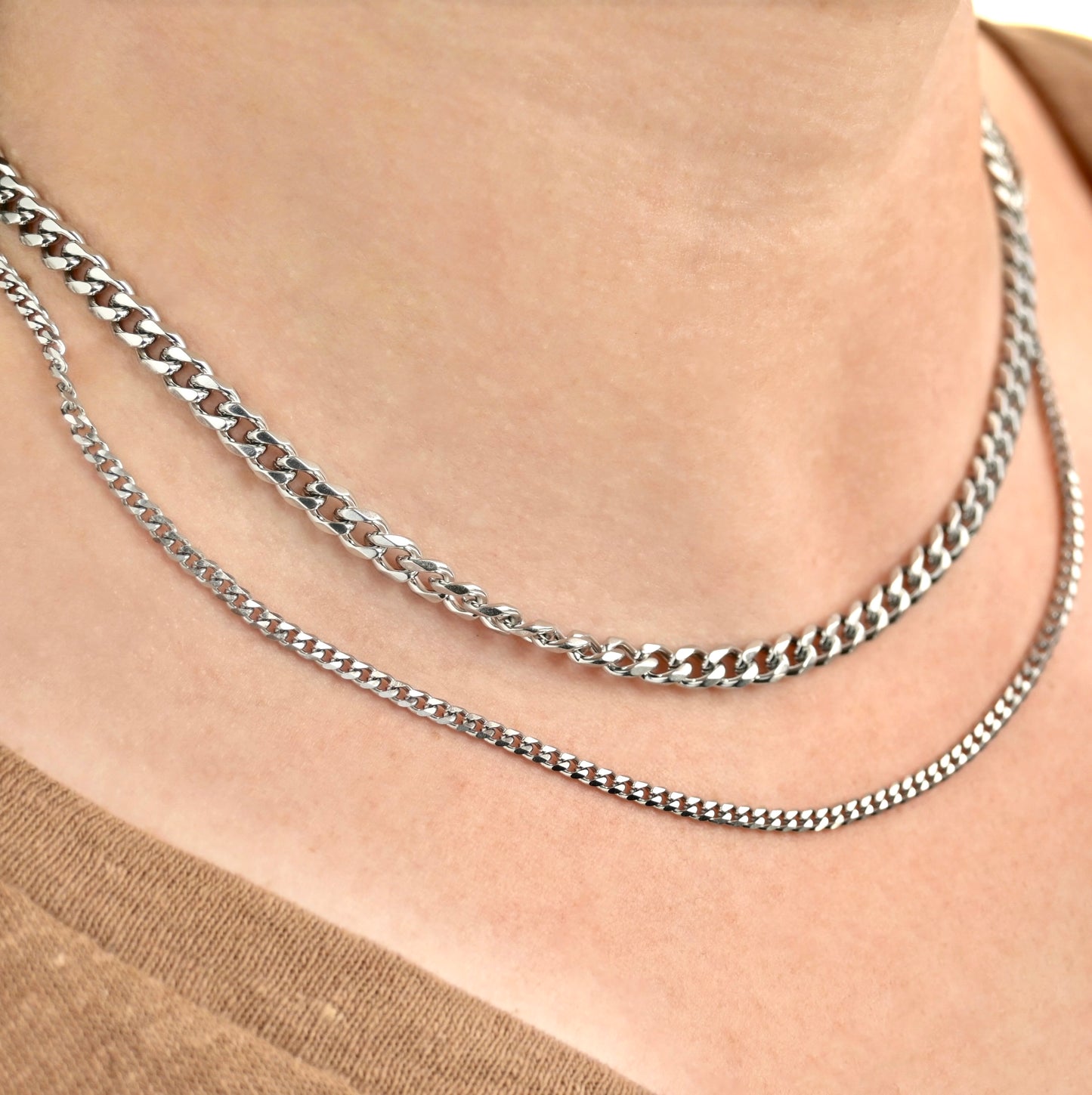 Two silver chain necklaces, one chunky 5mm and one dainty 3mm, on a person's neck against a neutral background