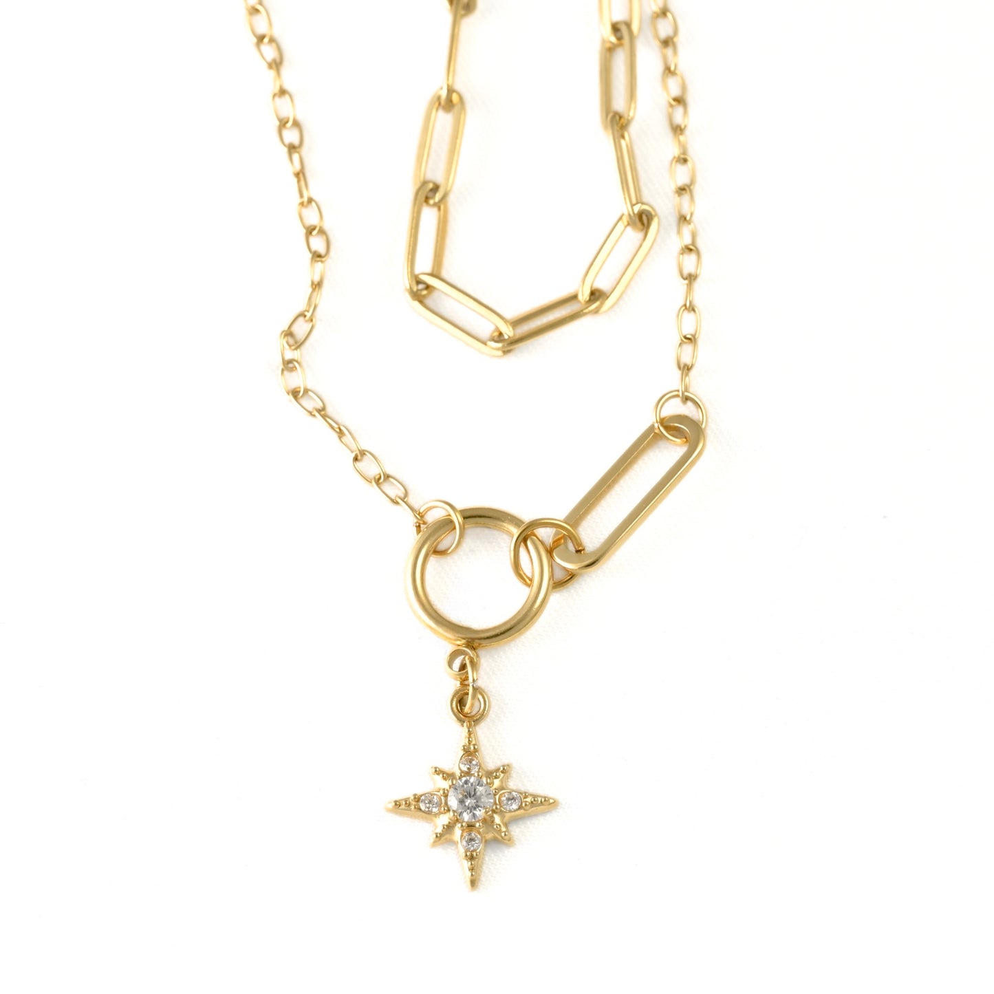 A gold-toned necklace featuring a paperclip-style chain, a ring connector, and a dangling starburst charm set with a clear gemstone, shown on a plain white background.