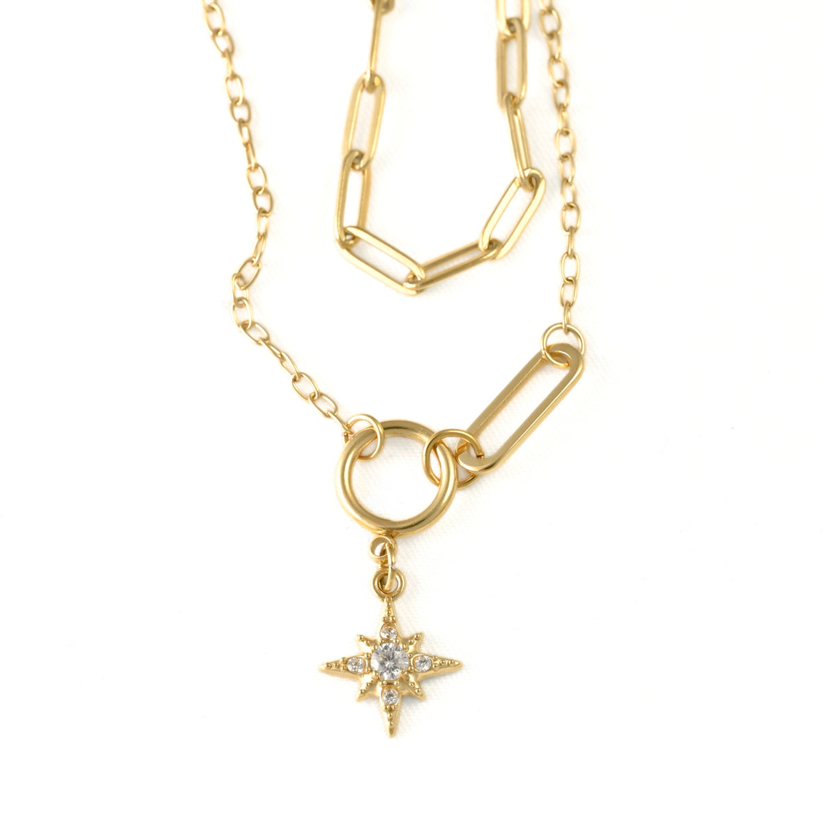 A gold-toned necklace featuring a paperclip-style chain, a ring connector, and a dangling starburst charm set with a clear gemstone, shown on a plain white background.