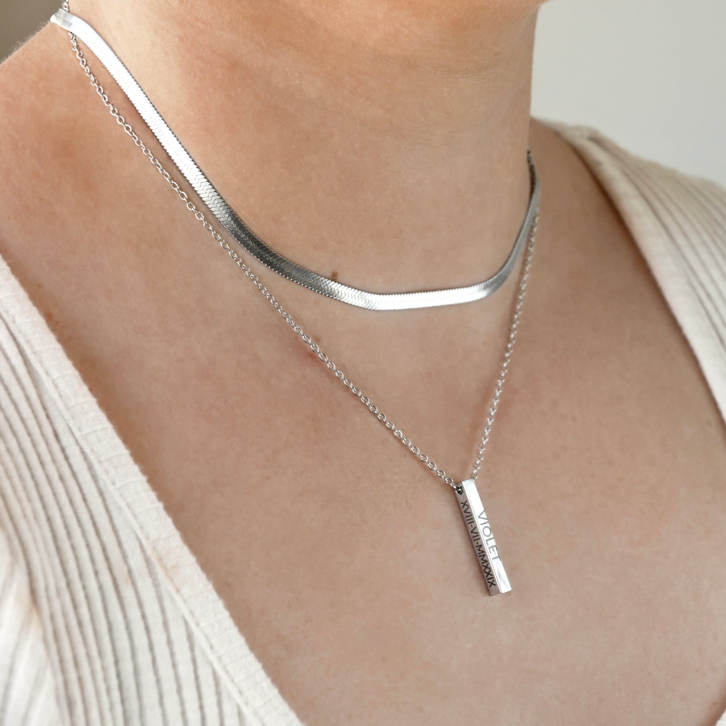 Silver 3d vertical pendant necklace on a person wearing a white top