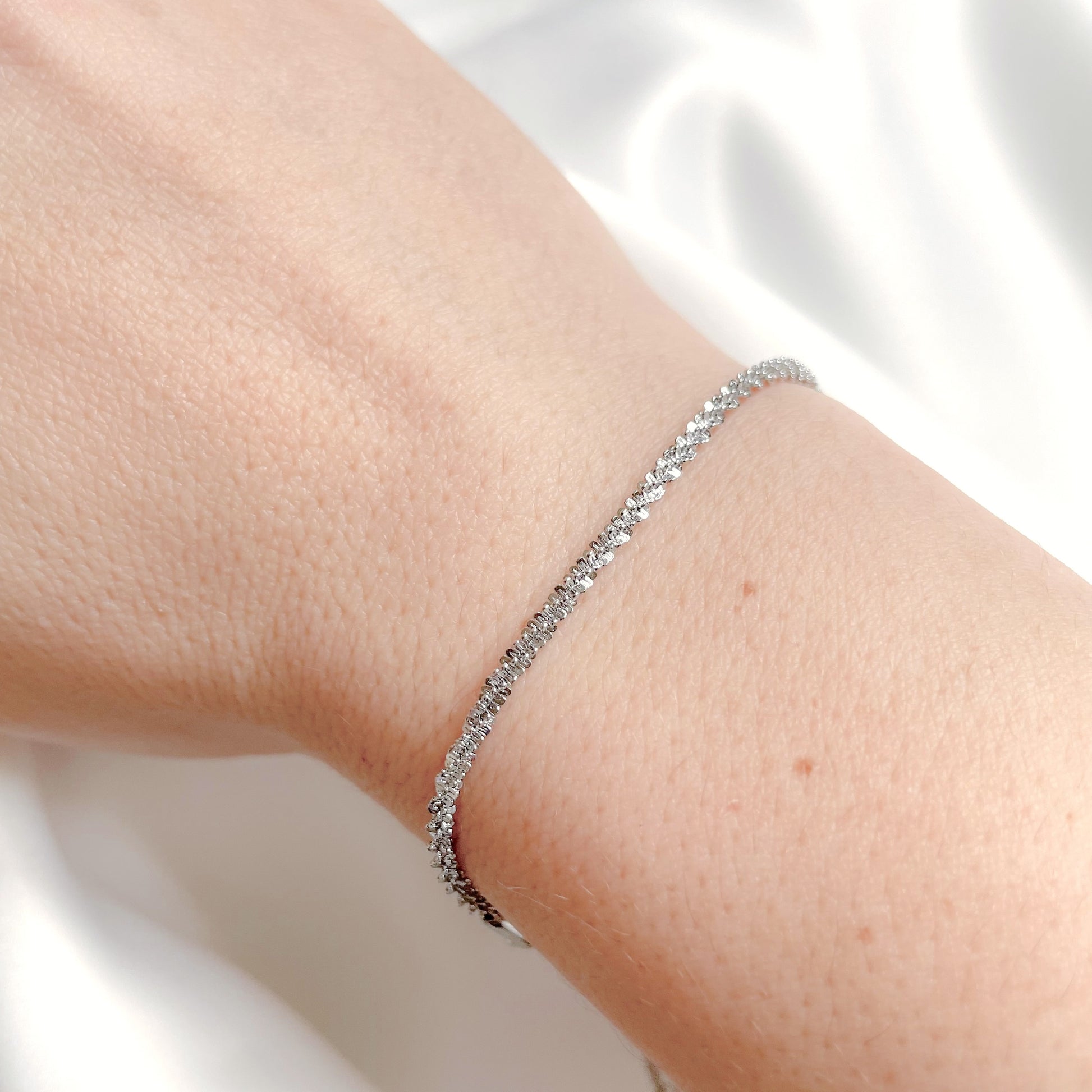 Dainty silver bracelet on a person's wrist with a light background