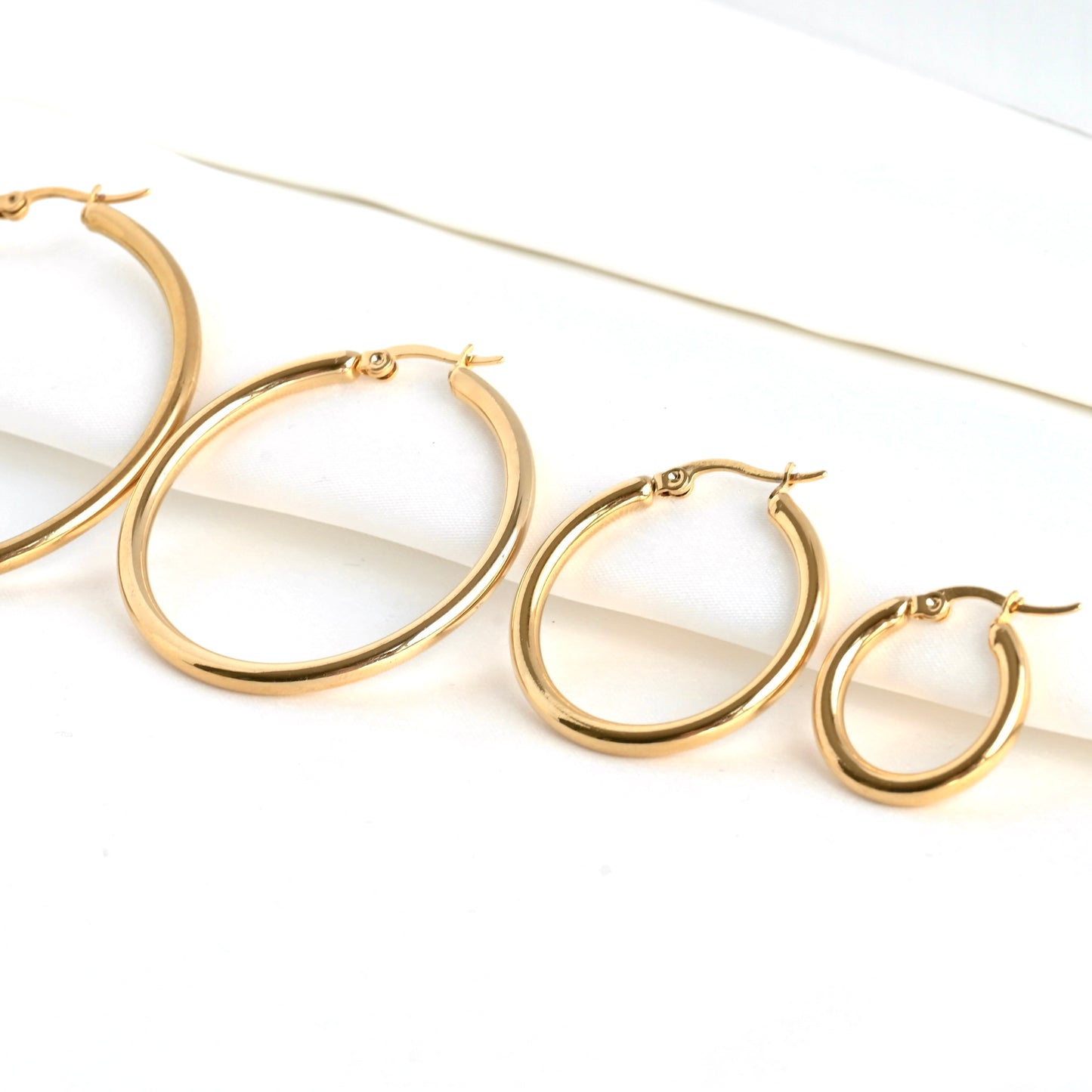 Gold hoop earrings of 4 different sizes from 20mm to 50mm side by side on a white background