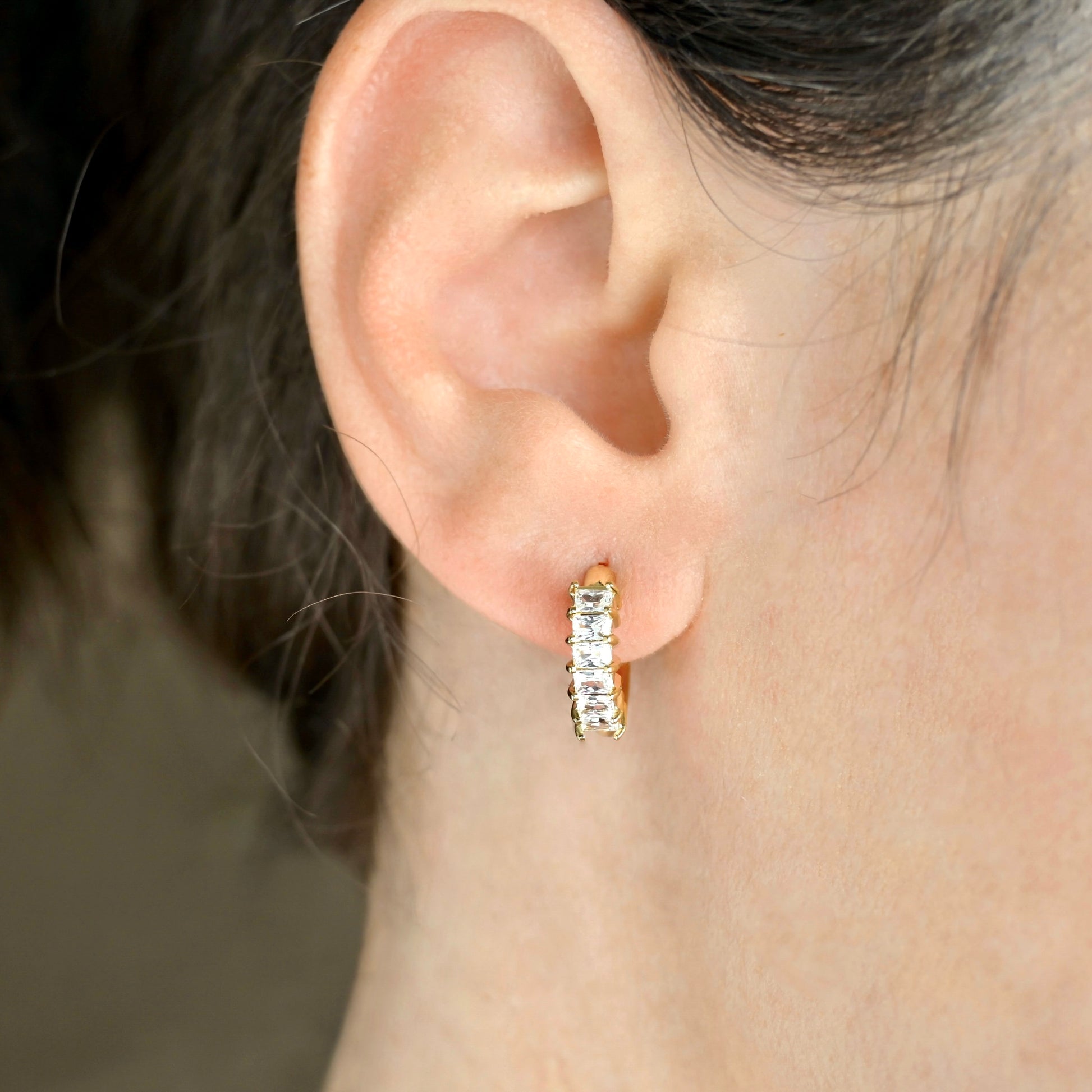 Close-up of an ear wearing a diamond gold hoop earring with a blurred background