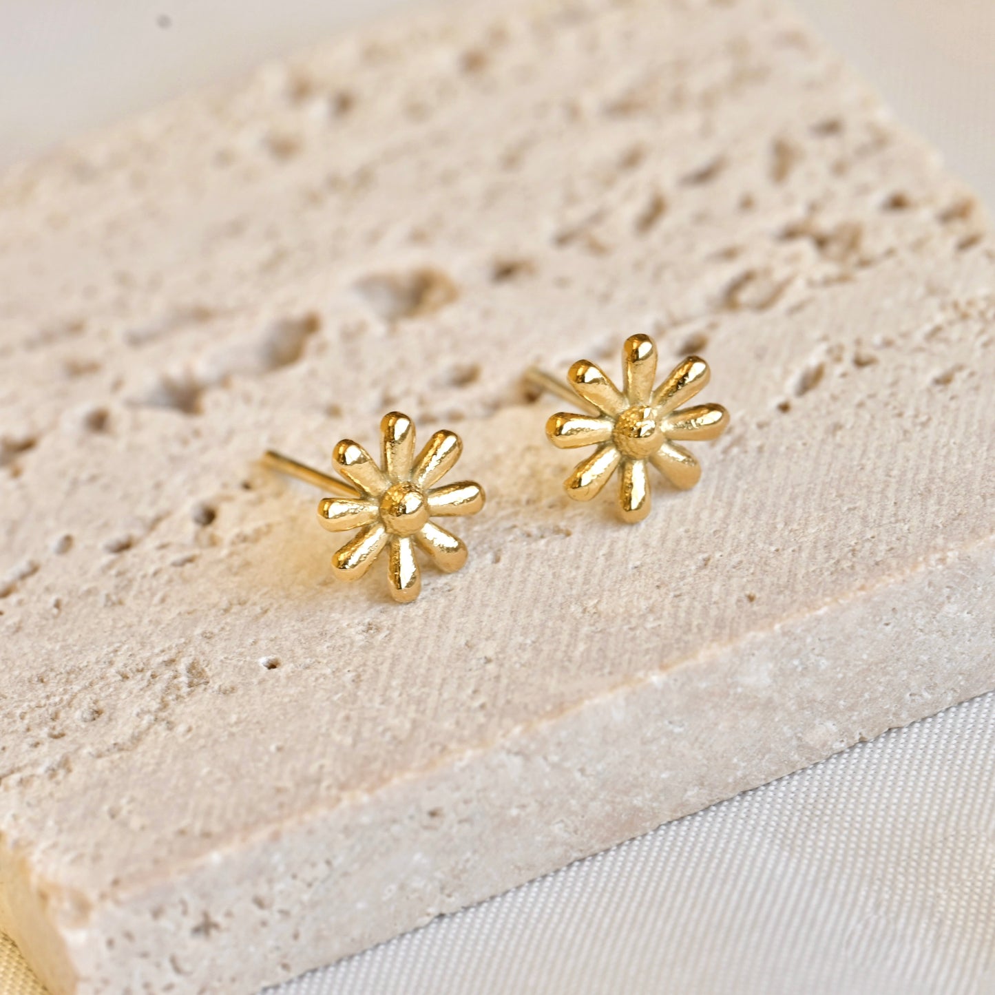 Gold flower-shaped earrings on a textured beige surface