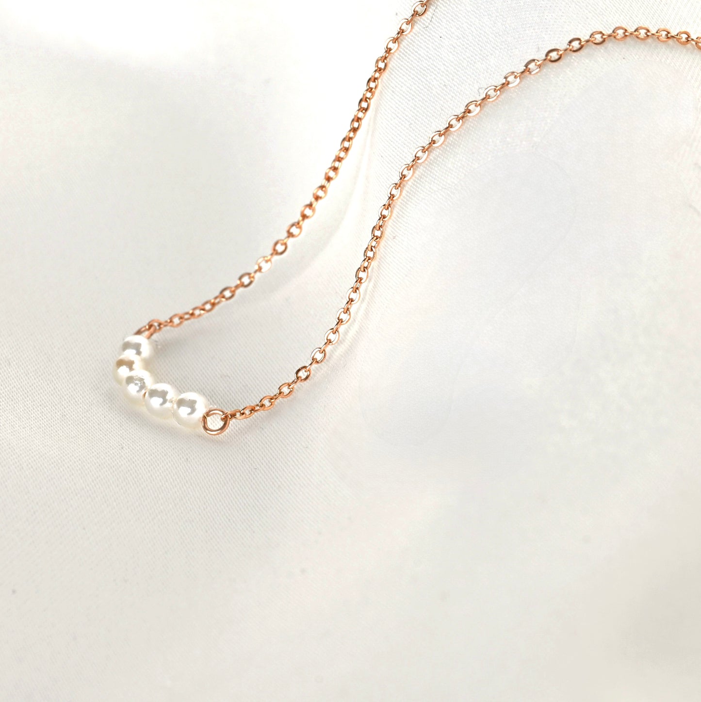 Close up side view of rose gold necklace with 5 tiny pearls forming a small curve on a light gray background