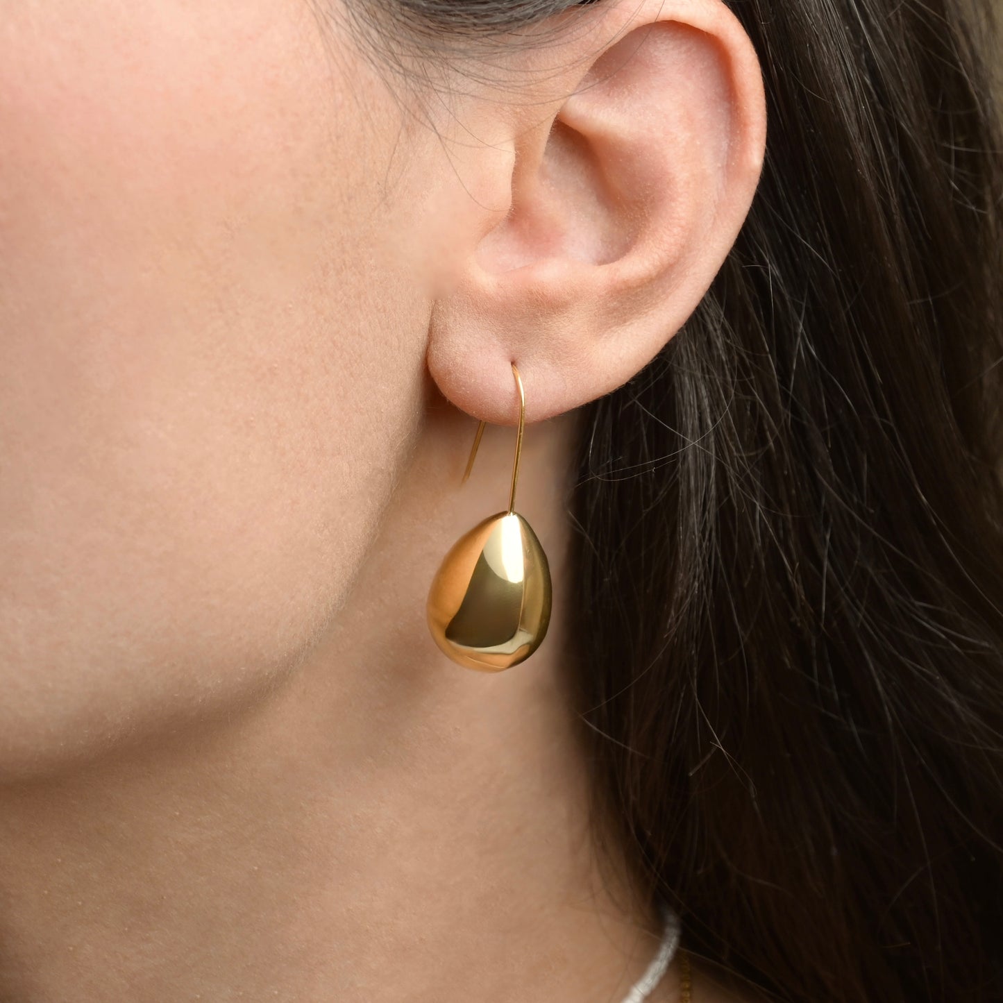 Gold teardrop earring with a hook worn by a person