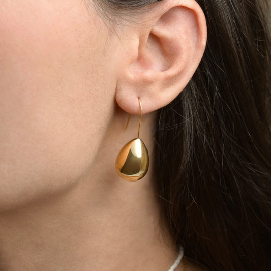Gold teardrop earring with a hook worn by a person