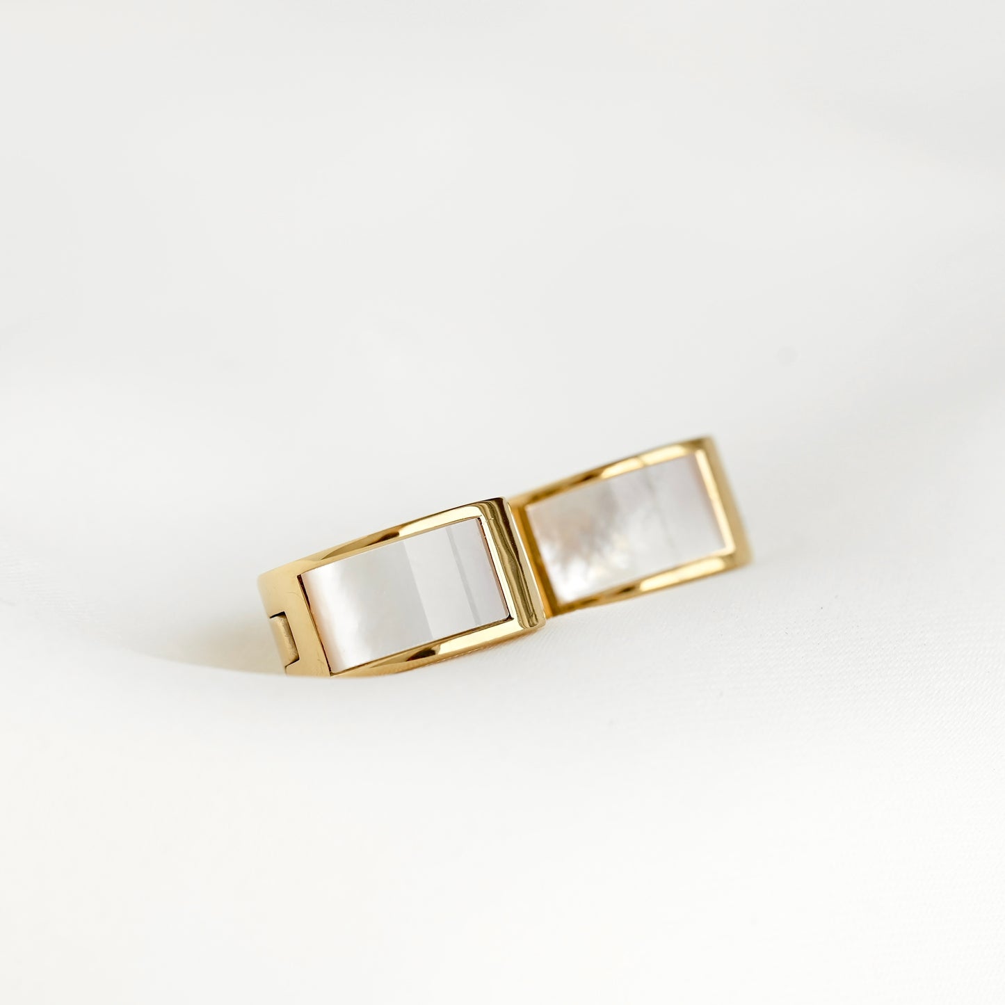 Gold-toned hoop earrings with two rectangular inlay panels made of iridescent white mother-of-pearl, photographed on a clean white background.