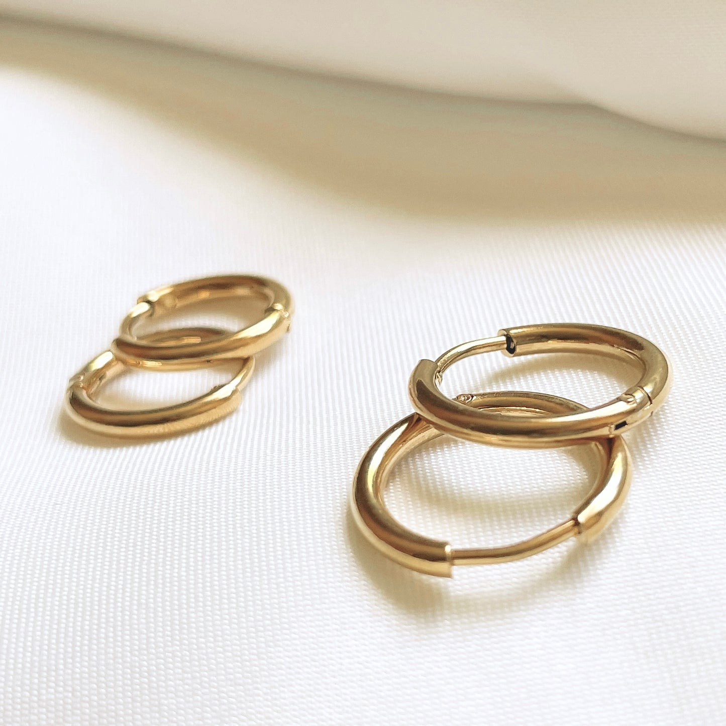 Pair of gold hoop earrings on a white fabric background under direct sunlight