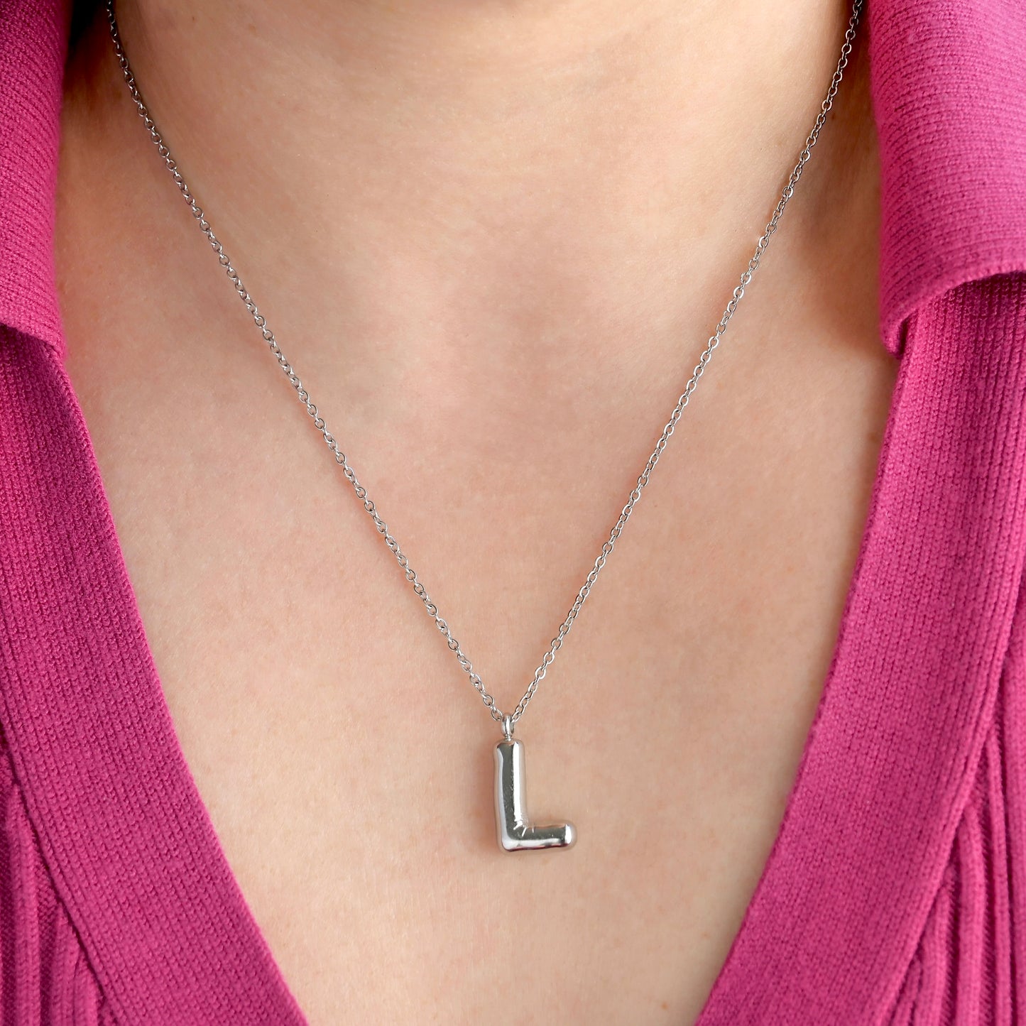 Silver necklace with a 'L' pendant worn by a person in a pink top.