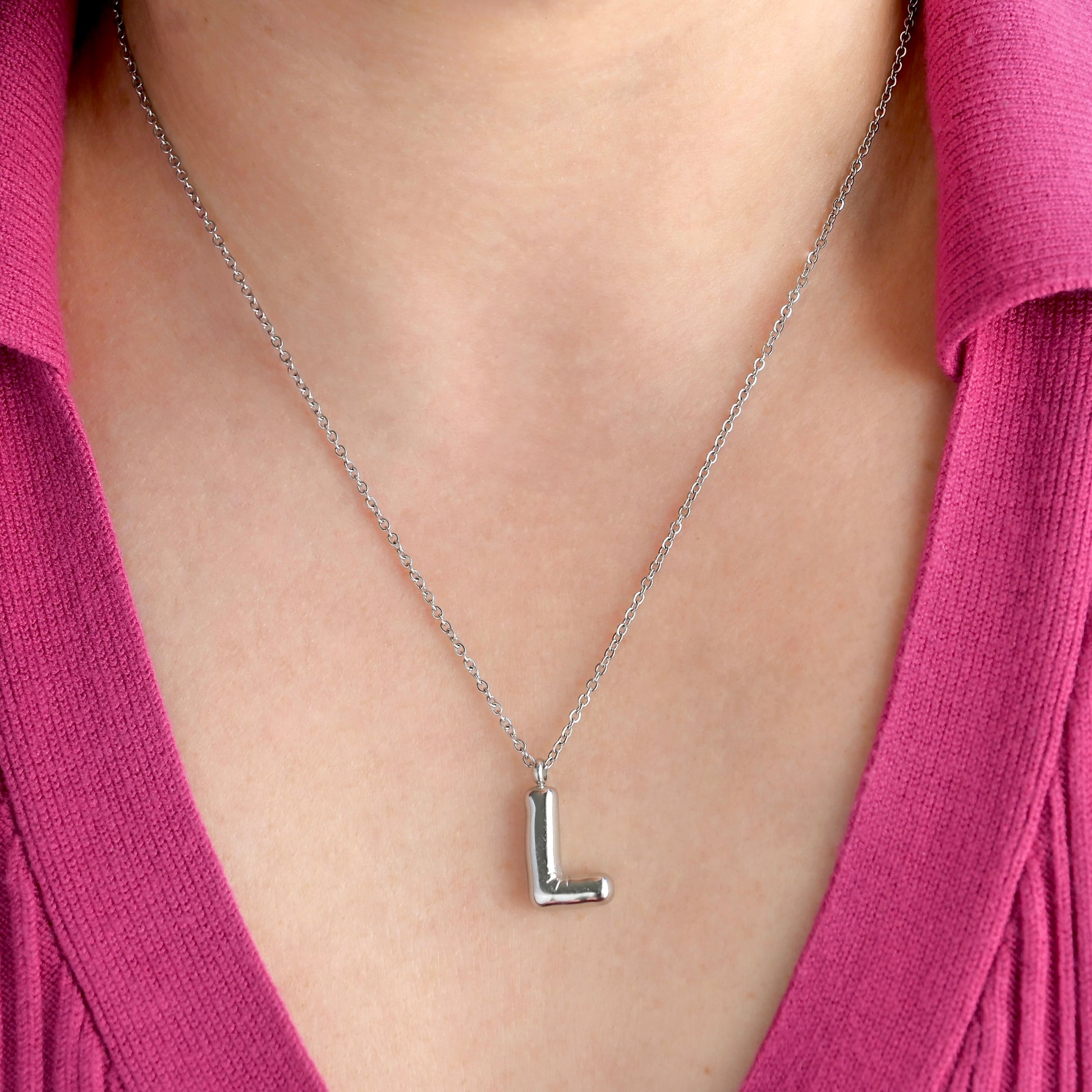 Silver necklace with a 'L' pendant worn by a person in a pink top.