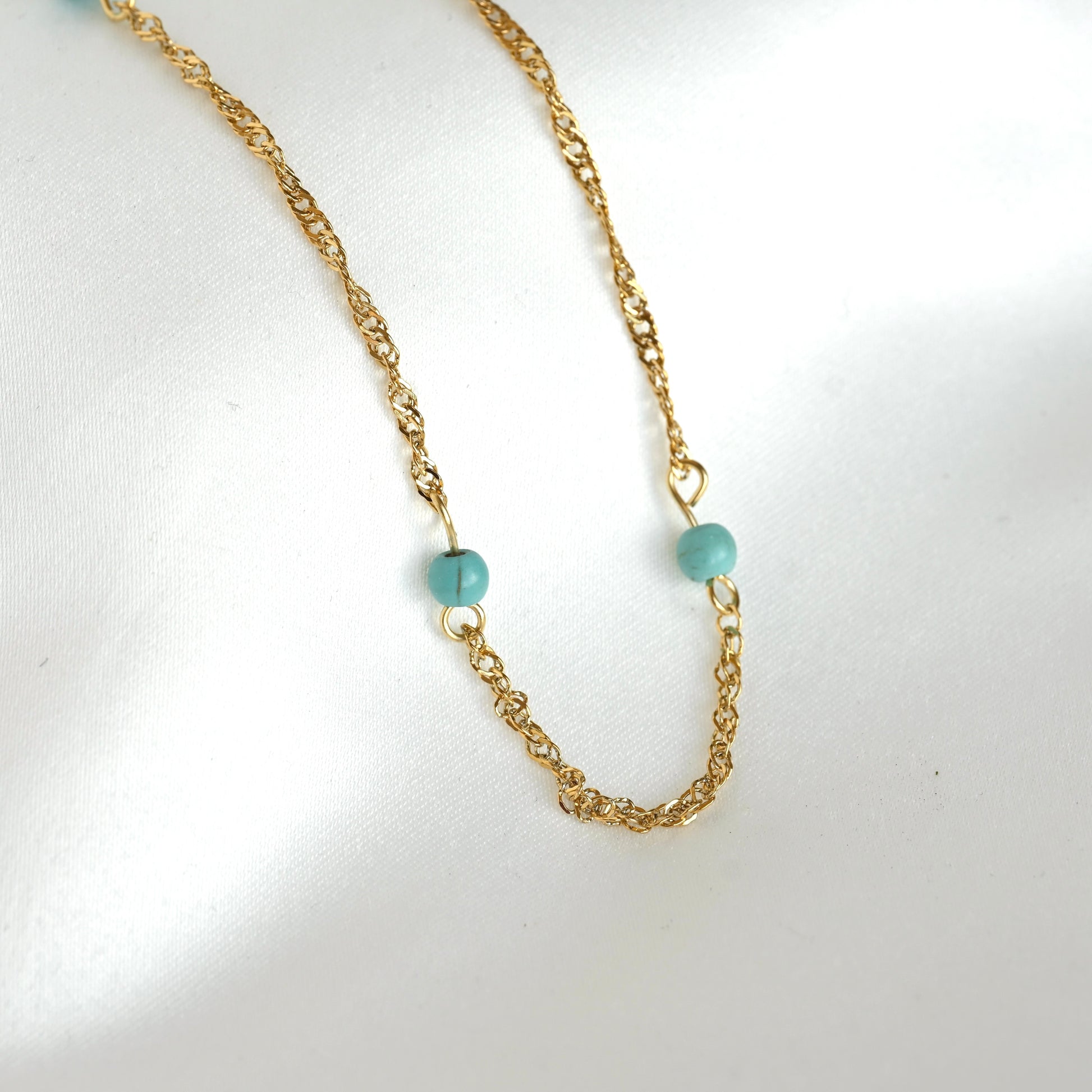 Gold twisted chain necklace with turquoise beads on a white background