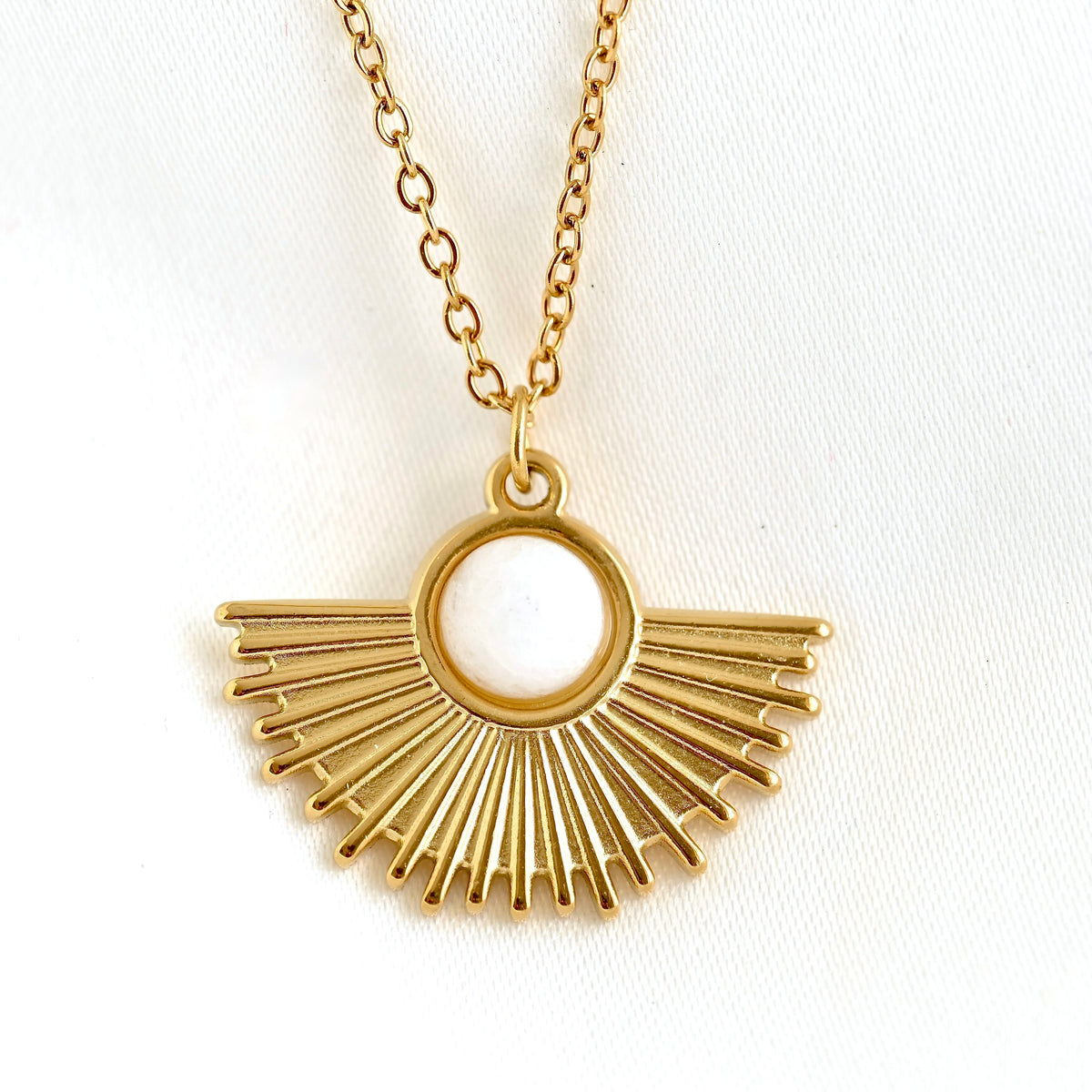 front view of gold fan pendant necklace with a white stone detail on a white background