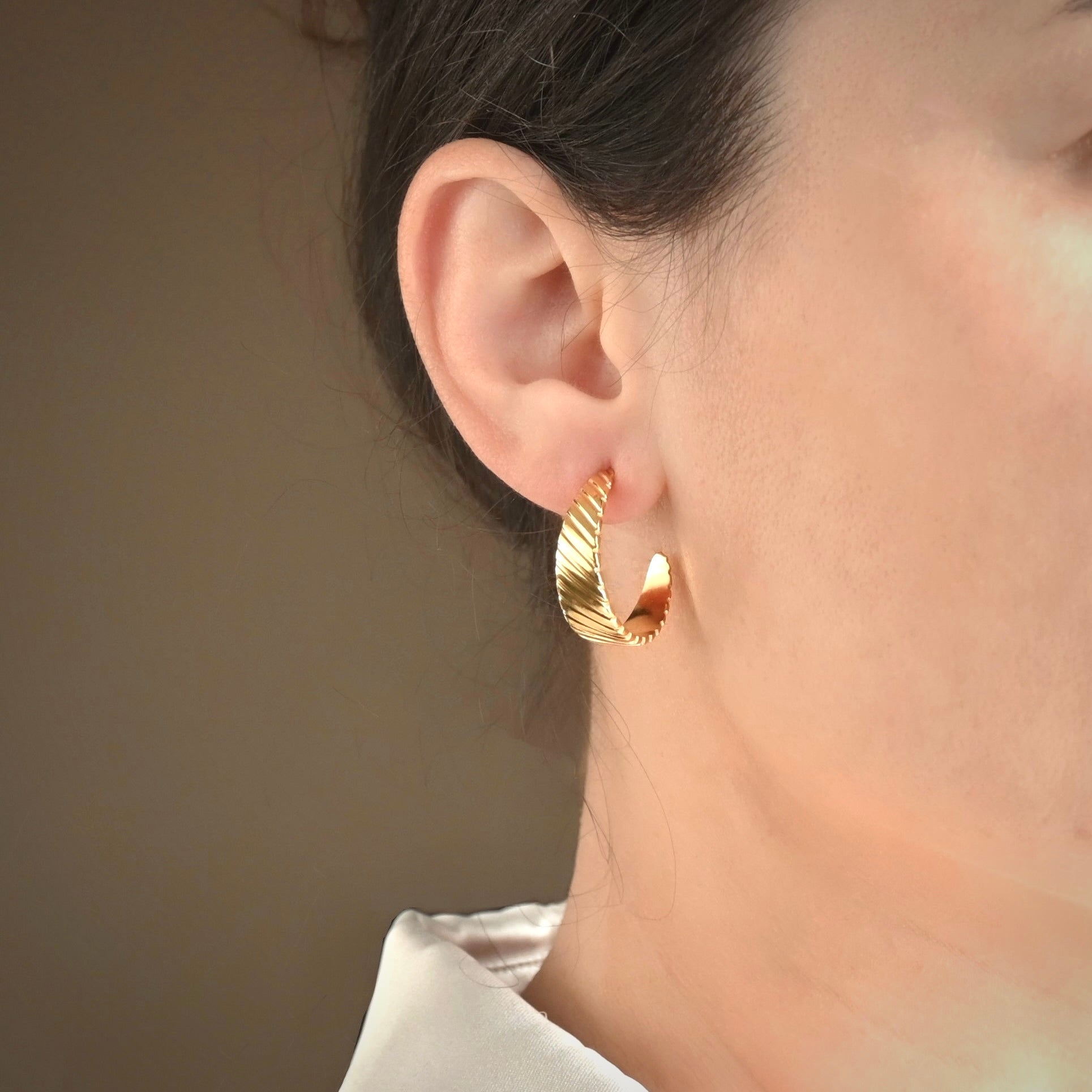 Ribbed croissant hoop earrings worn by a person with a neutral background