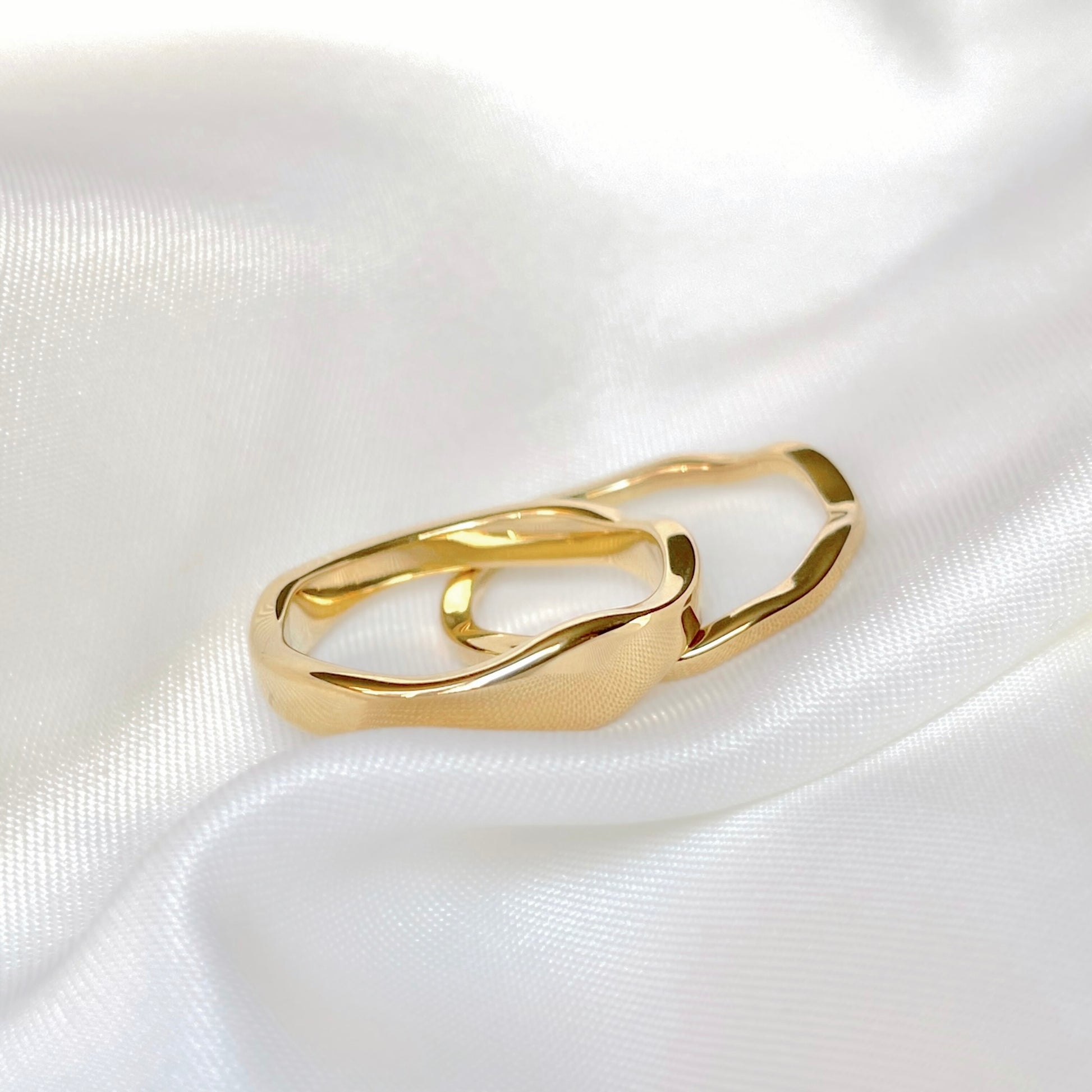 Close up view of gold molten wave rings on a white satin background