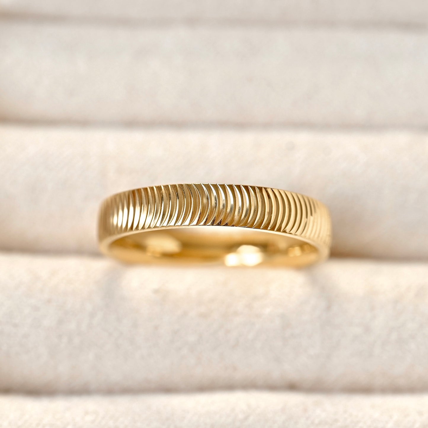 A gold band ring with a textured, ridged outer surface and a polished inner band, displayed on a soft beige velvet ring box.