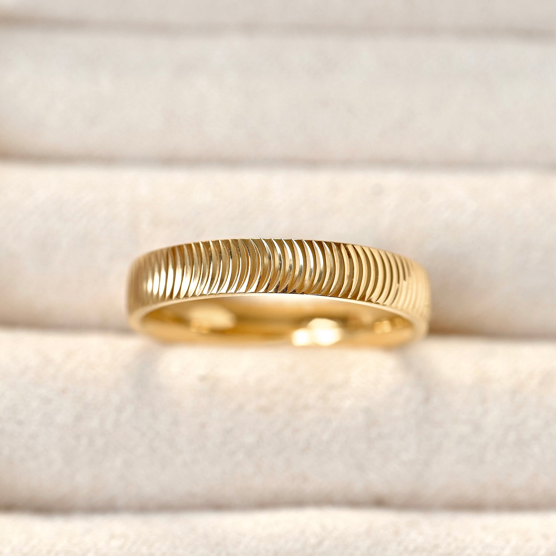 A gold band ring with a textured, ridged outer surface and a polished inner band, displayed on a soft beige velvet ring box.