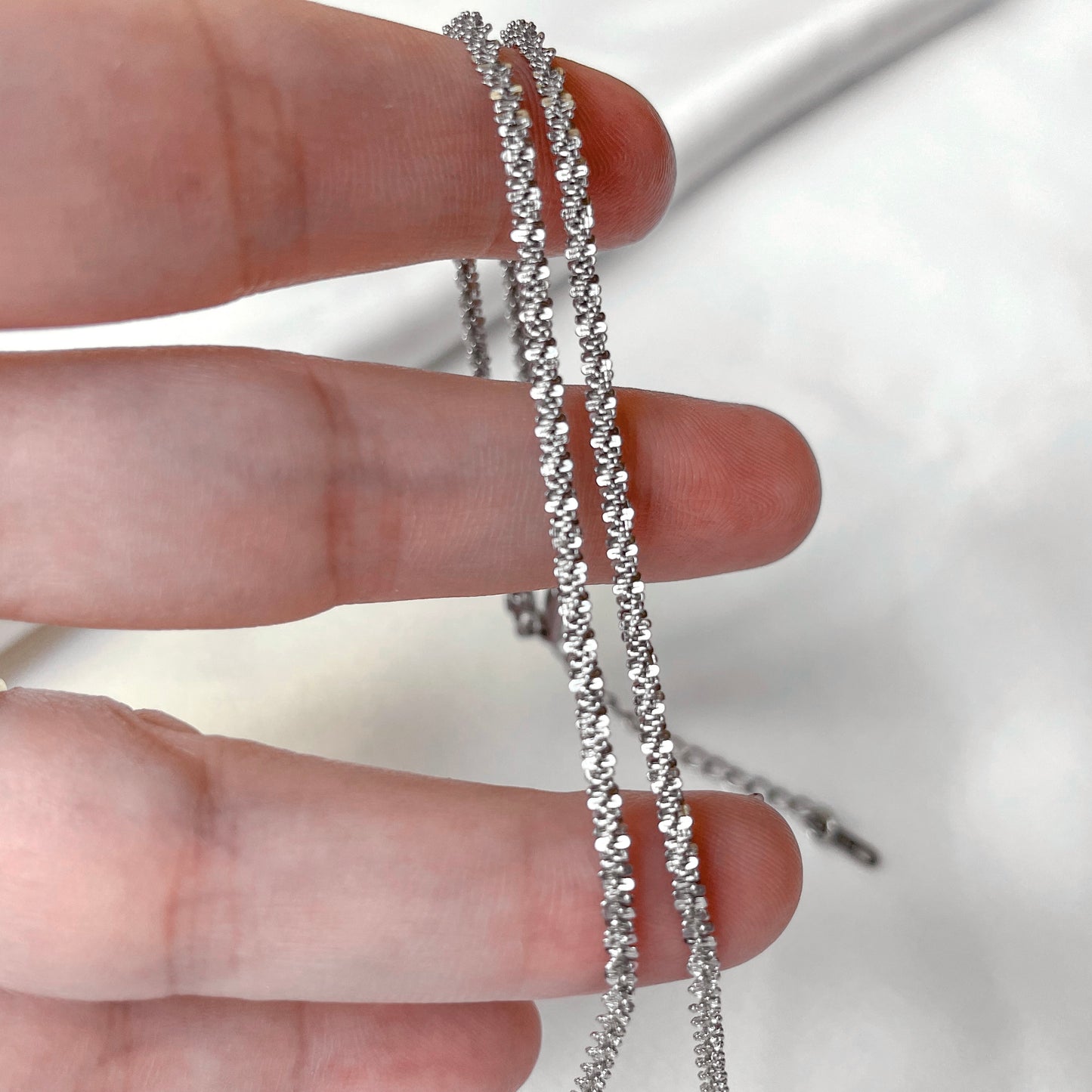 Silver popcorn chain held between fingers against a neutral background