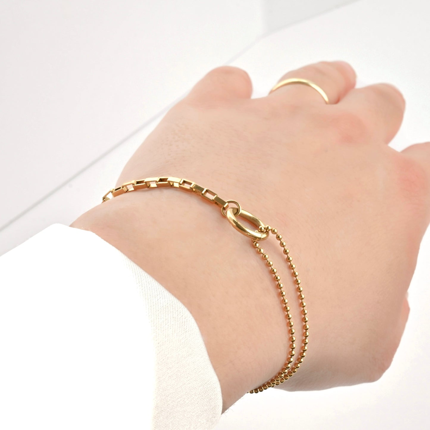 Gold chain bracelet on a wrist with a plain background
