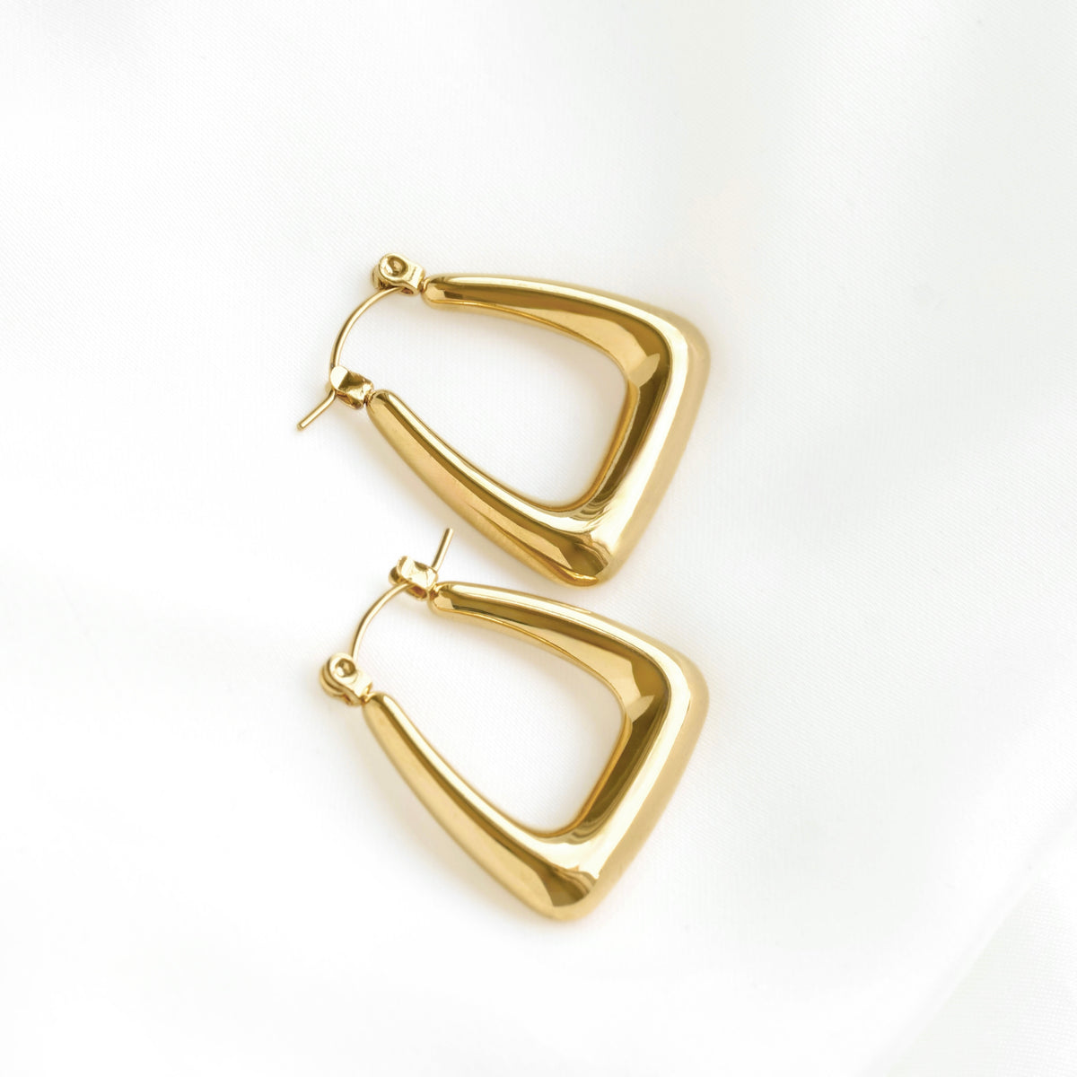 A pair of gold-toned geometric hoop earrings with a polished, rounded triangular shape, displayed on a clean white background.