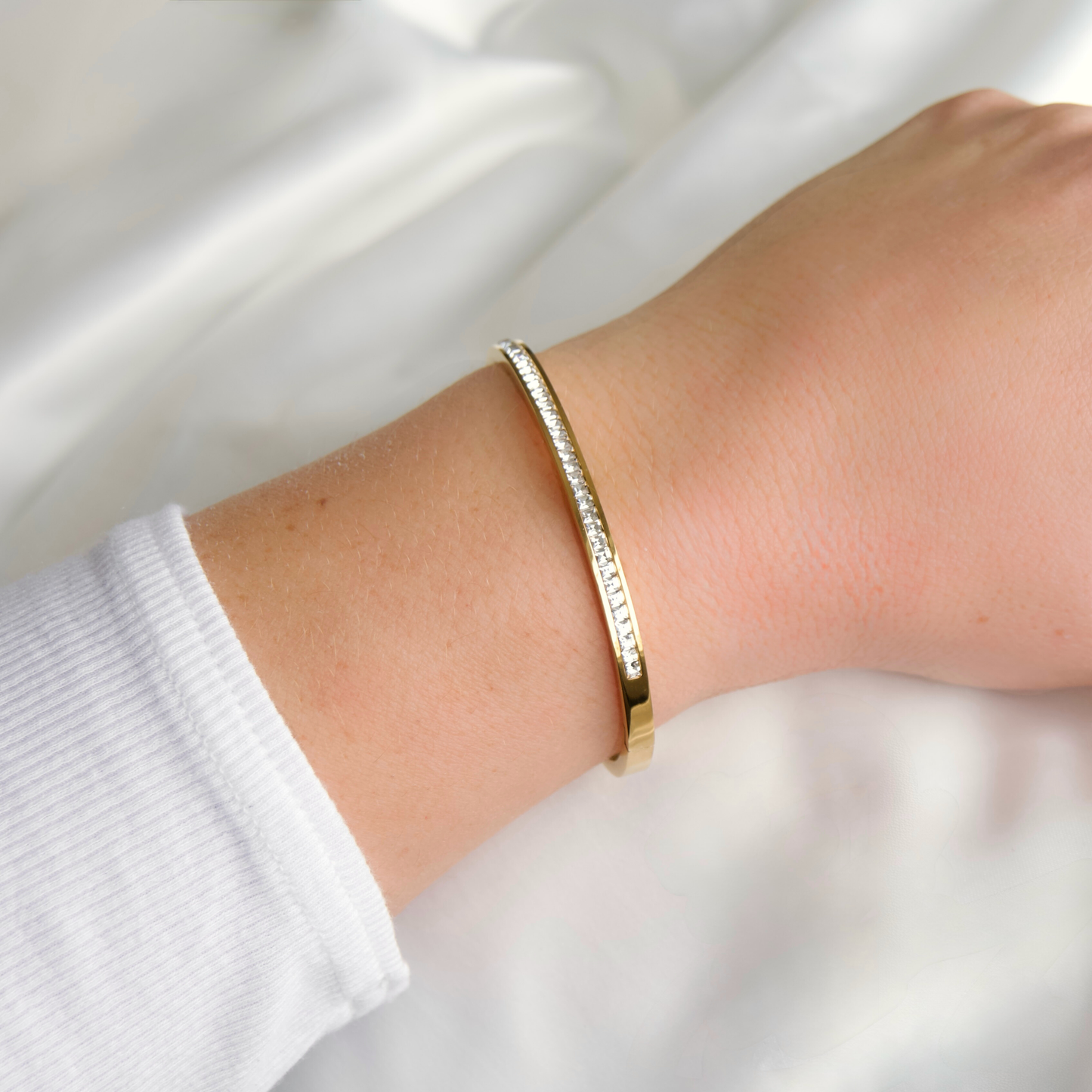 Gold hinged bangle bracelet  with diamonds on a person's wrist with a white background