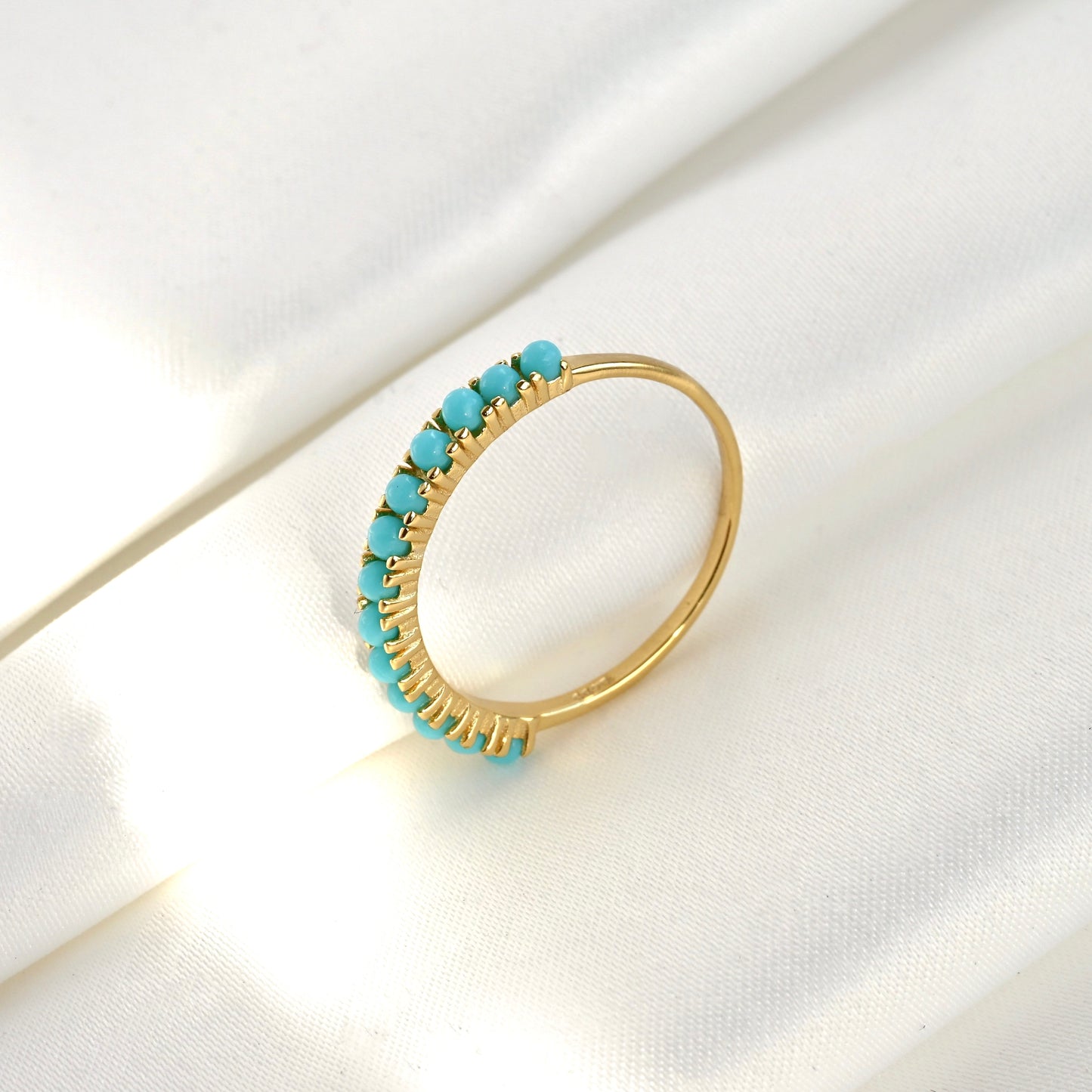 Gold ring with turquoise stones leaning upright against a folded white fabric, the turquoise stones faicng left side.