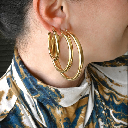 Thick gold hoop earrings in large(50mm), medium(40mm) and small(30mm) sizes worn on an ear.