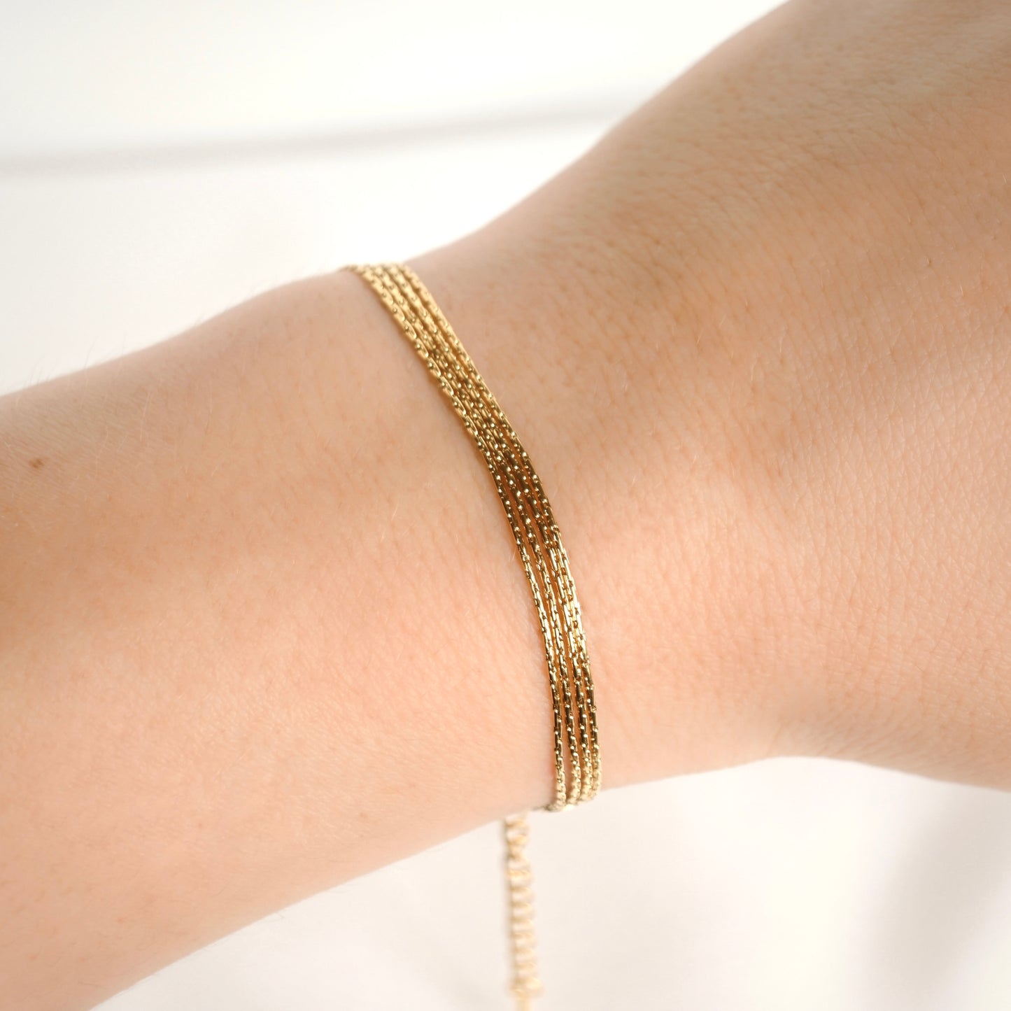 Layered gold chain bracelet on a person's wrist against a white background