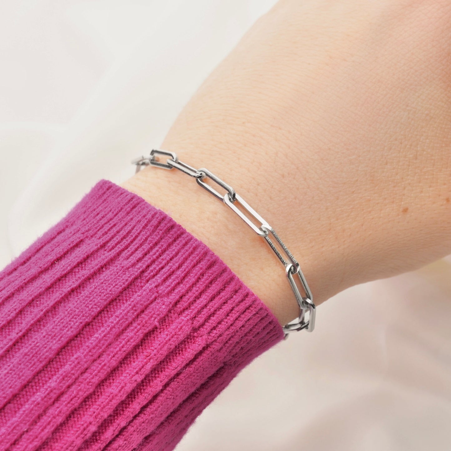 Silver rectangular link chain bracelet on a wrist with a pink sleeve against a neutral background