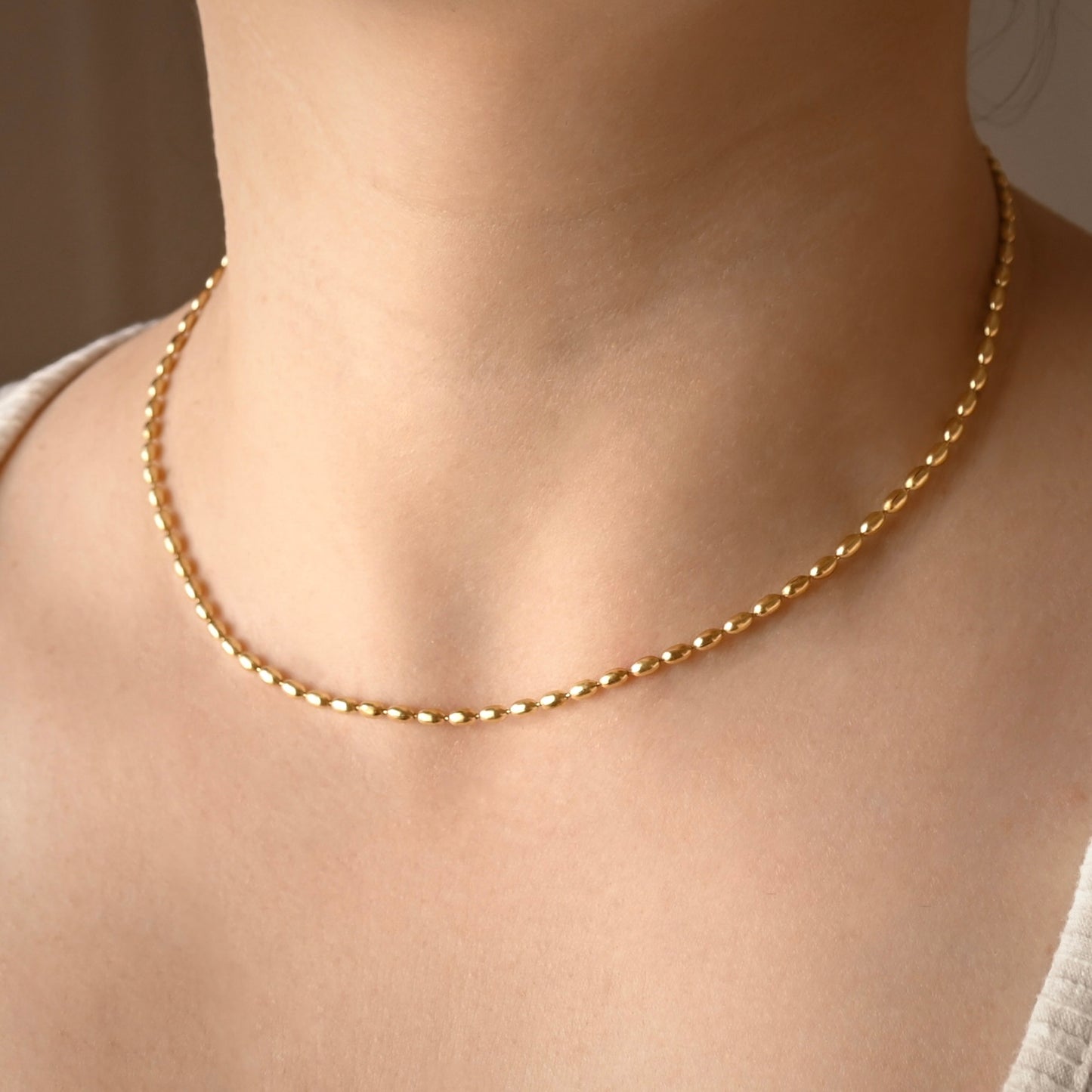 Dainty gold chain necklace  with puffed oval links on a person's neck with a neutral background