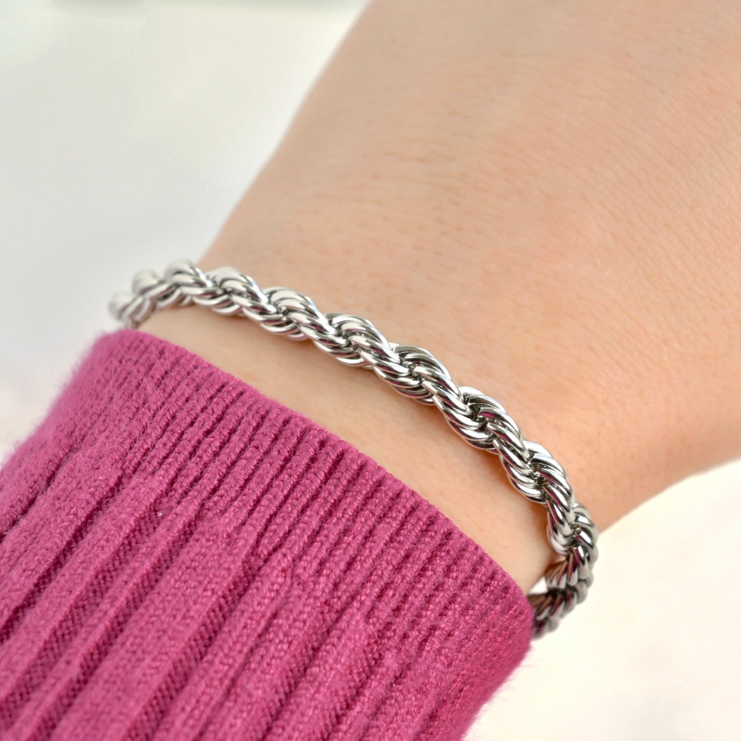 Close-up view of chunky silver rope chain bracelet on a wrist with a pink sleeve against a white background