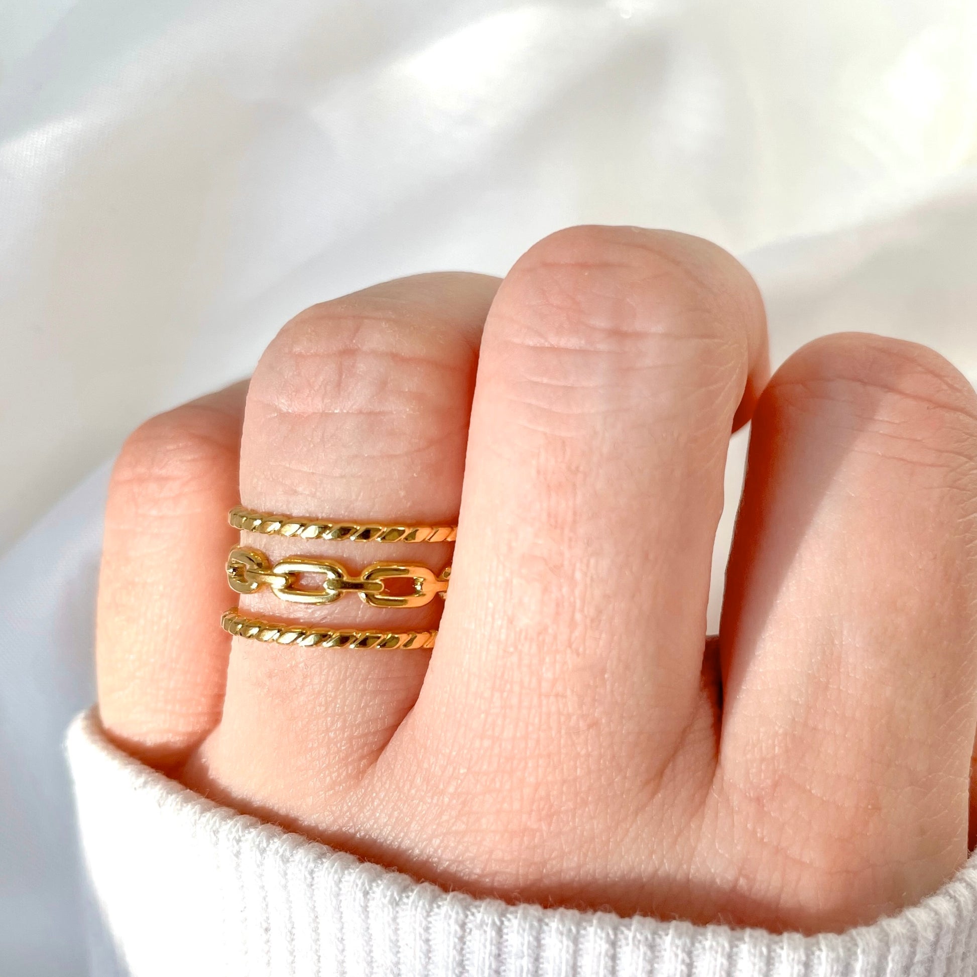 Adjustable gold chain-link ring on a finger against a white background