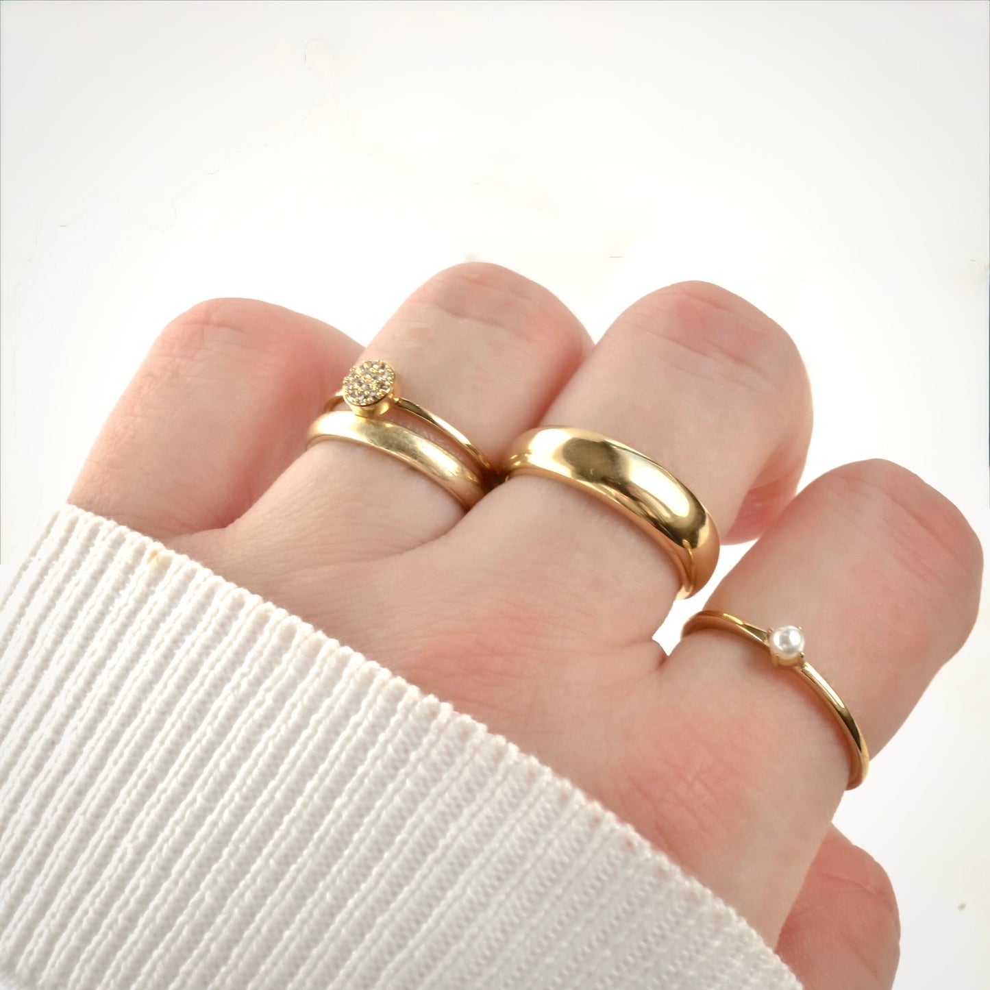 Gold rings stacked on a person's fingers in a fist pose with a white background