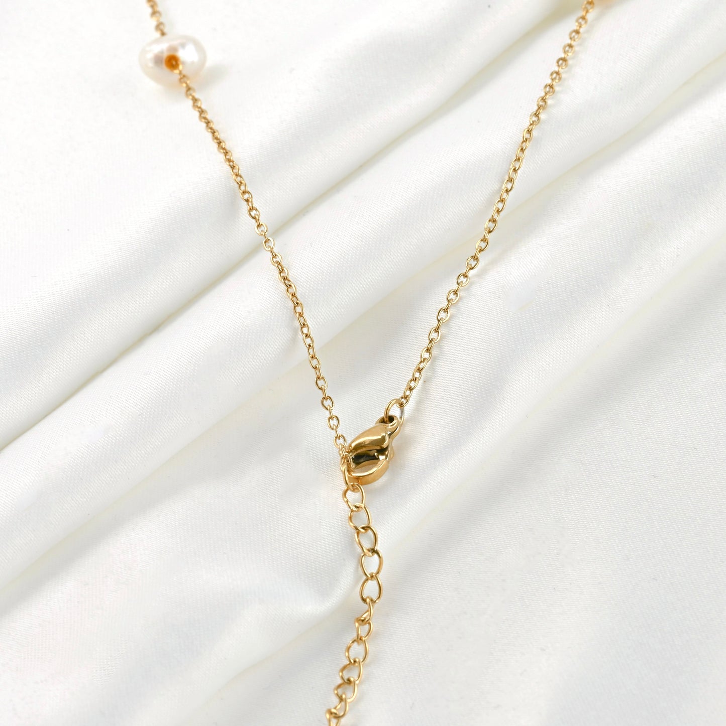 Close up view of the lobster claw clasp and extender of gold pearl chain necklace on a white fabric background 