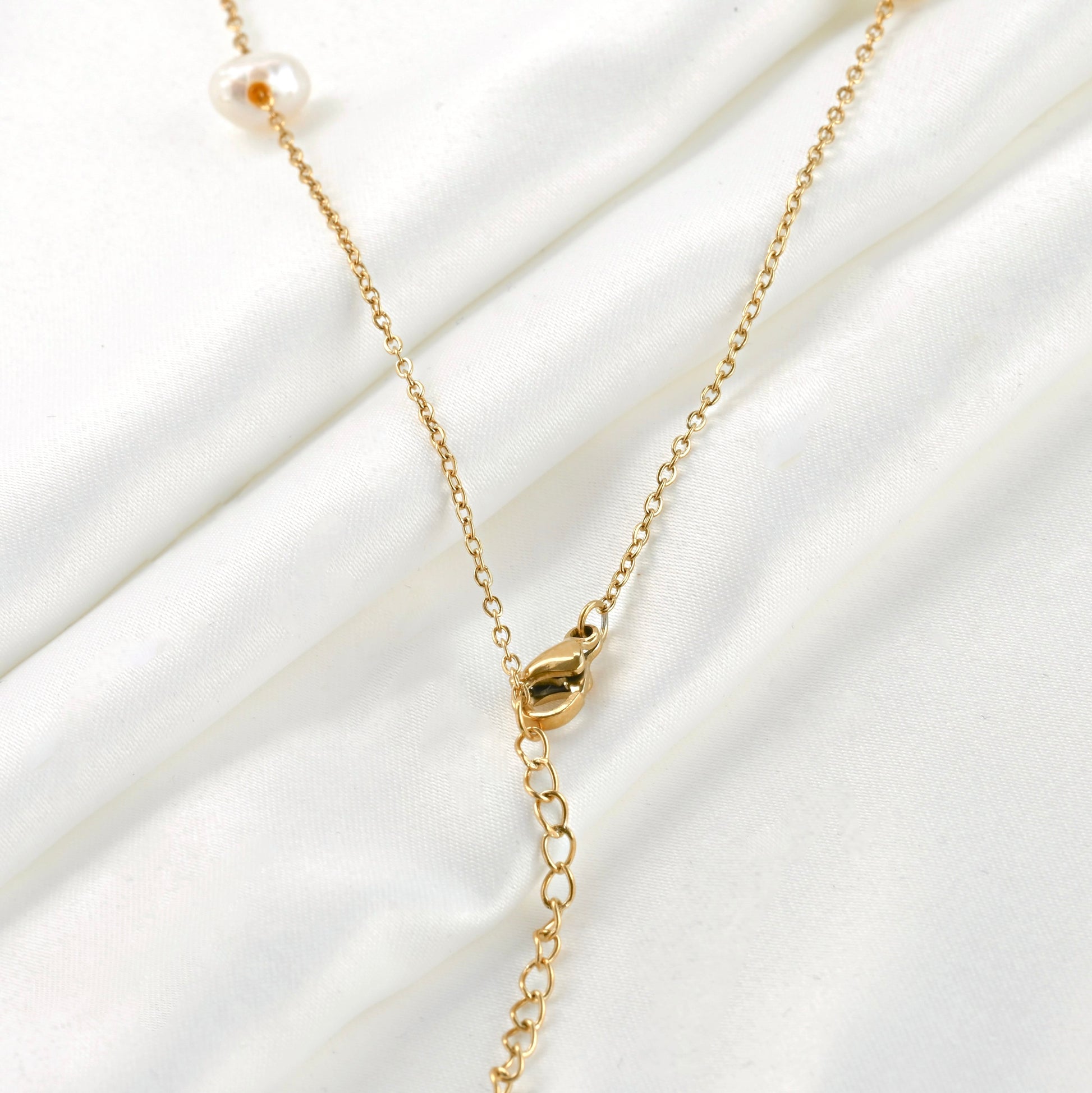 Close up view of the lobster claw clasp and extender of gold pearl chain necklace on a white fabric background 