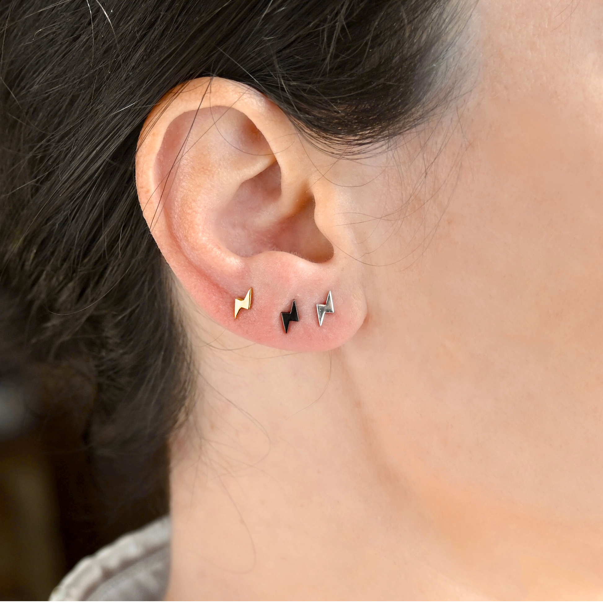 Close-up of an ear wearing three lightning bolt stud earrings in gold, black and silver